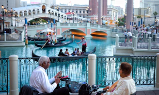 Gondolas float on canal with people watching from bench