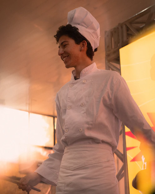 Young chef in white uniform smiles while cooking