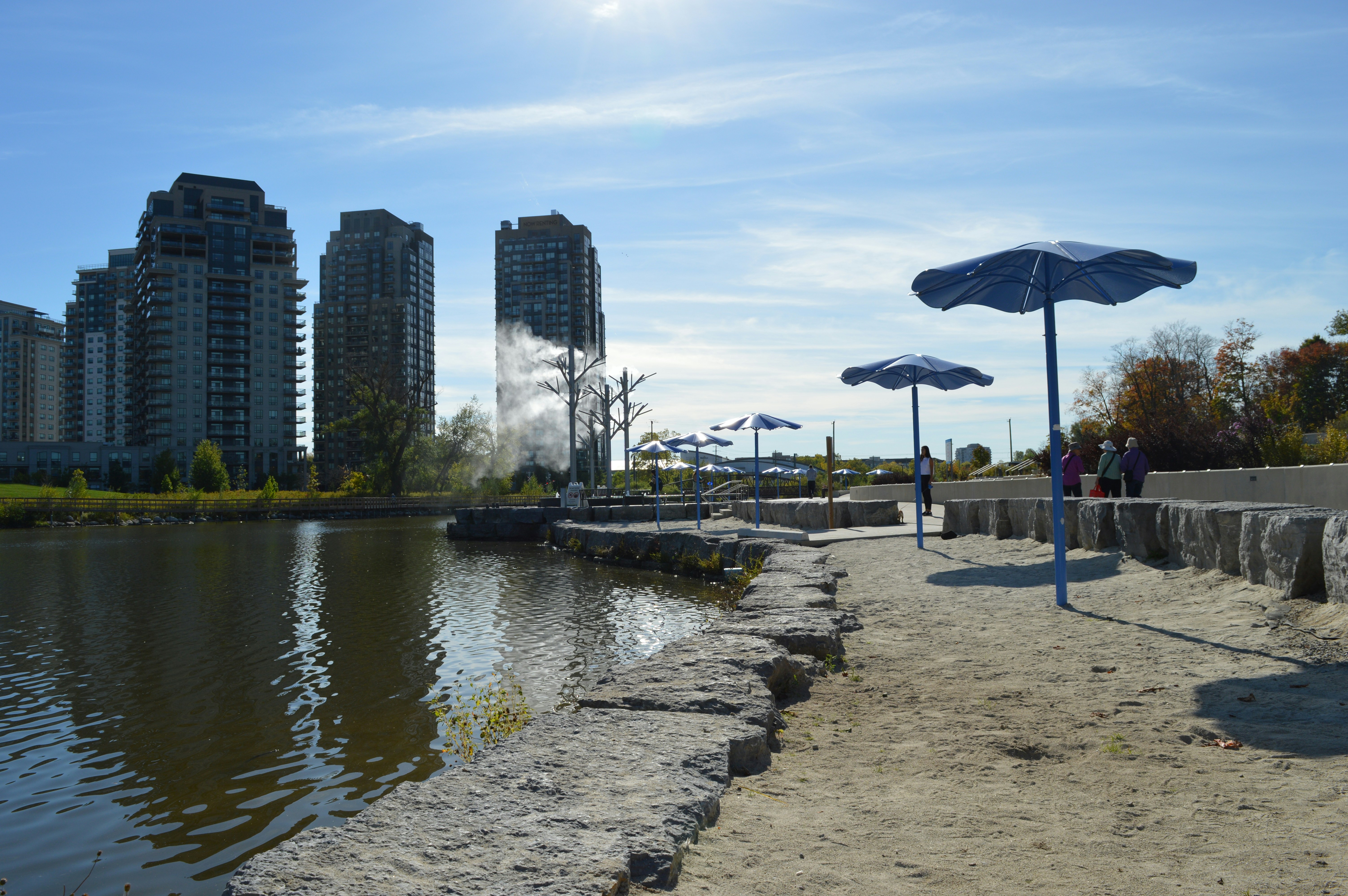 Stop image for Luxury Rockies Passage: Calgary to Kelowna in 3 Days - Beach umbrellas and buildings by a calm lake. -  in Western Canada - Photo by Emily Wassmansdorf on Unsplash