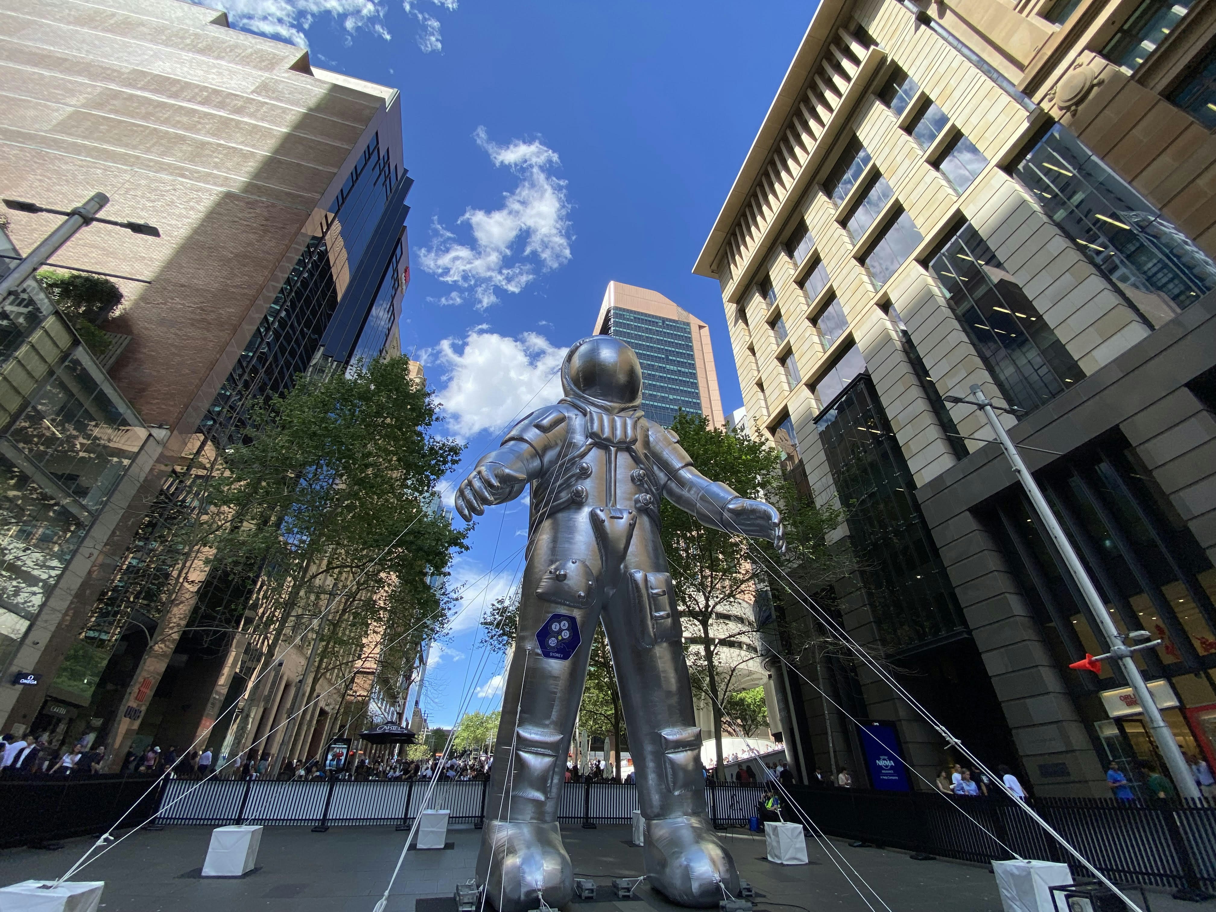 Astronaut statue between modern buildings under blue sky.