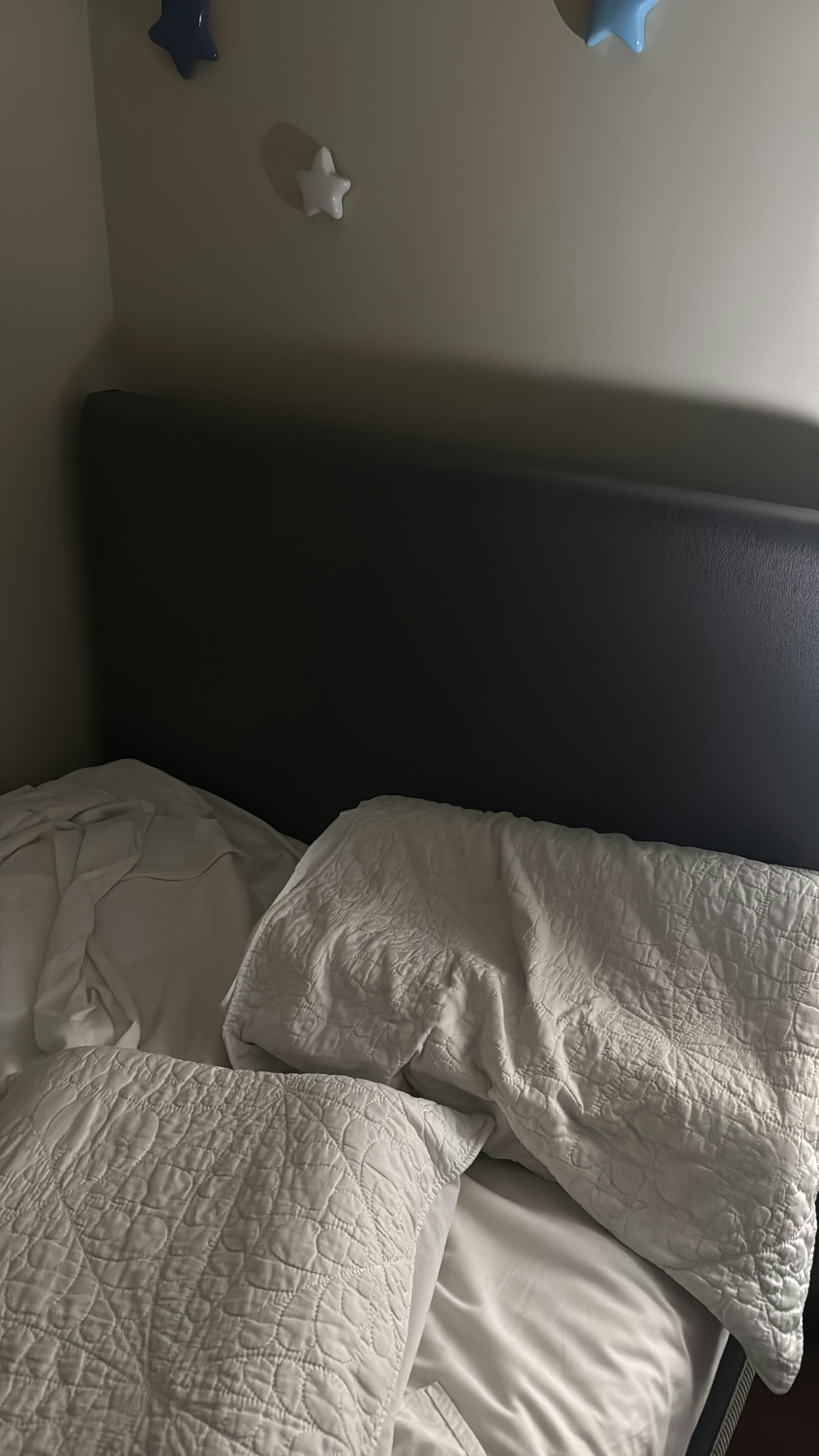 Unmade bed with pillows and blankets near a headboard.