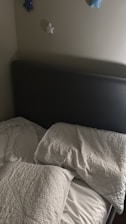 Unmade bed with pillows and blankets near a headboard.