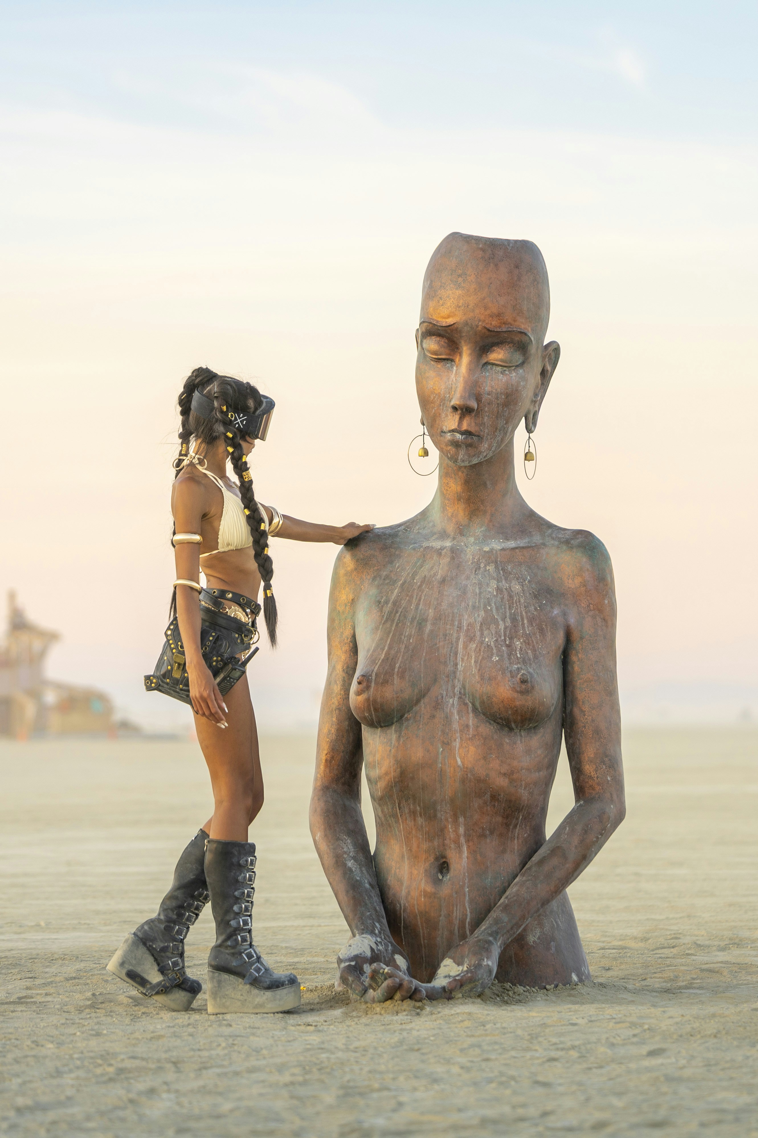 Woman touches large weathered statue in desert landscape.