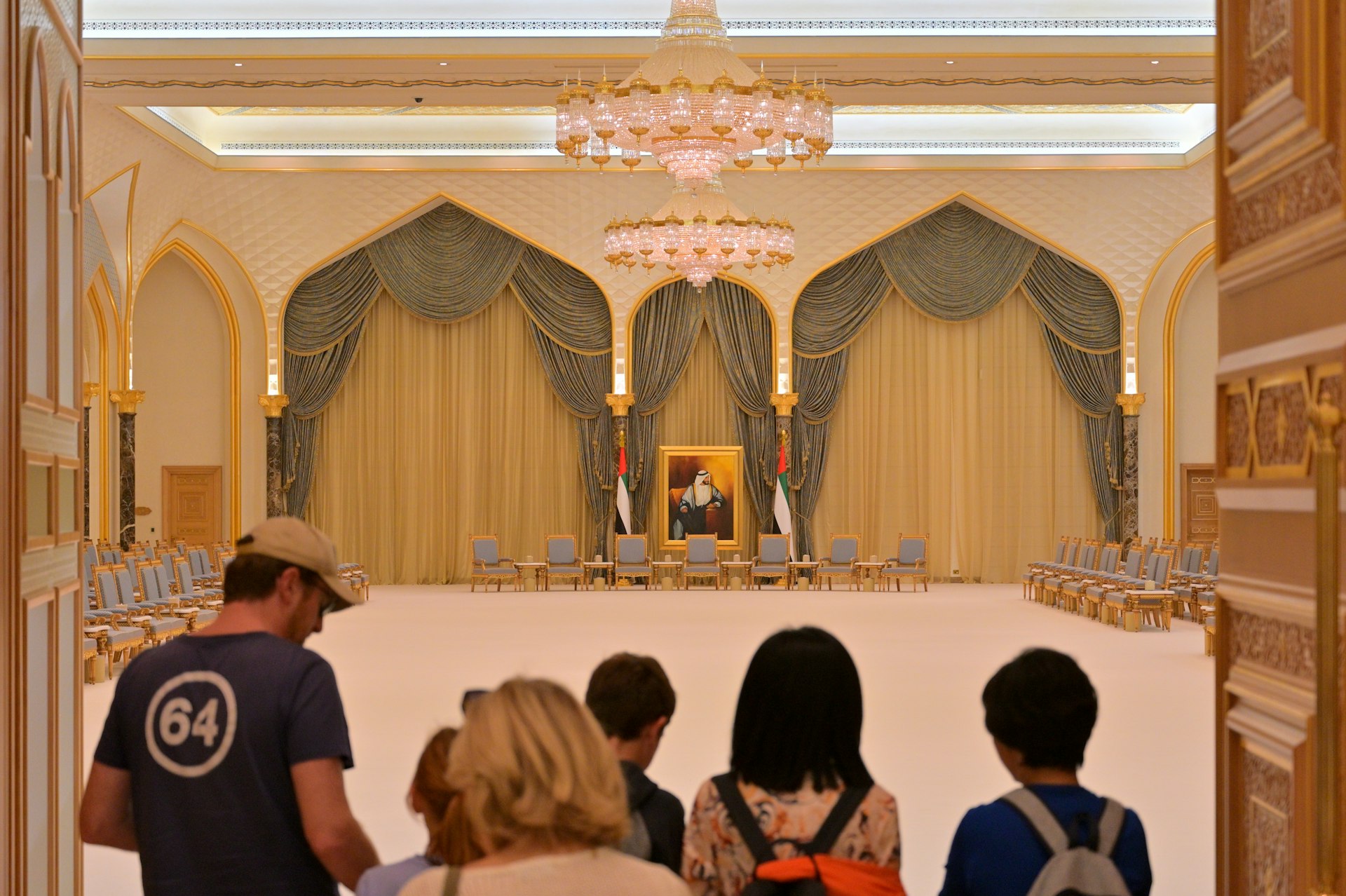 Tourists view a grand hall with a portrait and portrait.