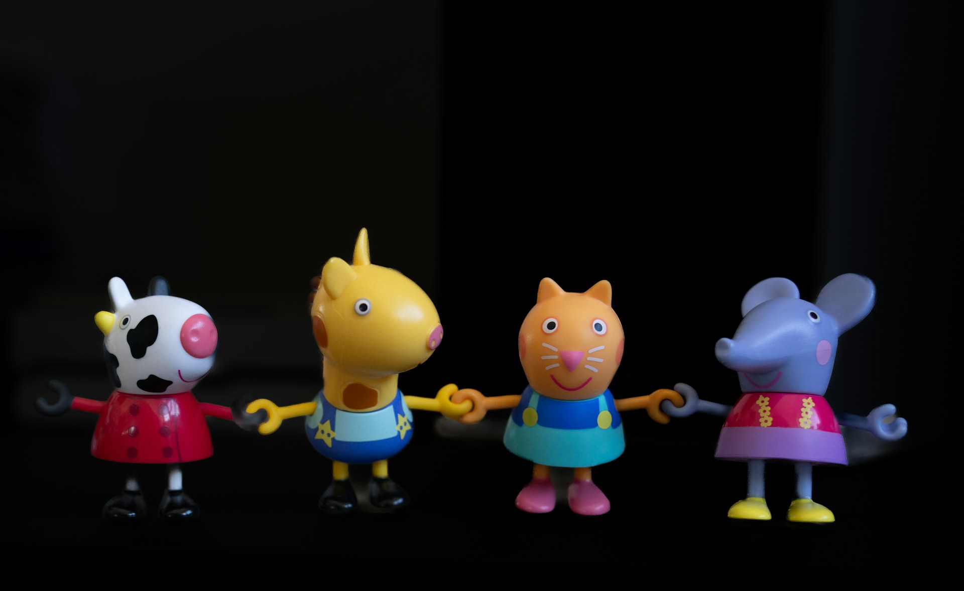 Four cartoon animal toys holding hands