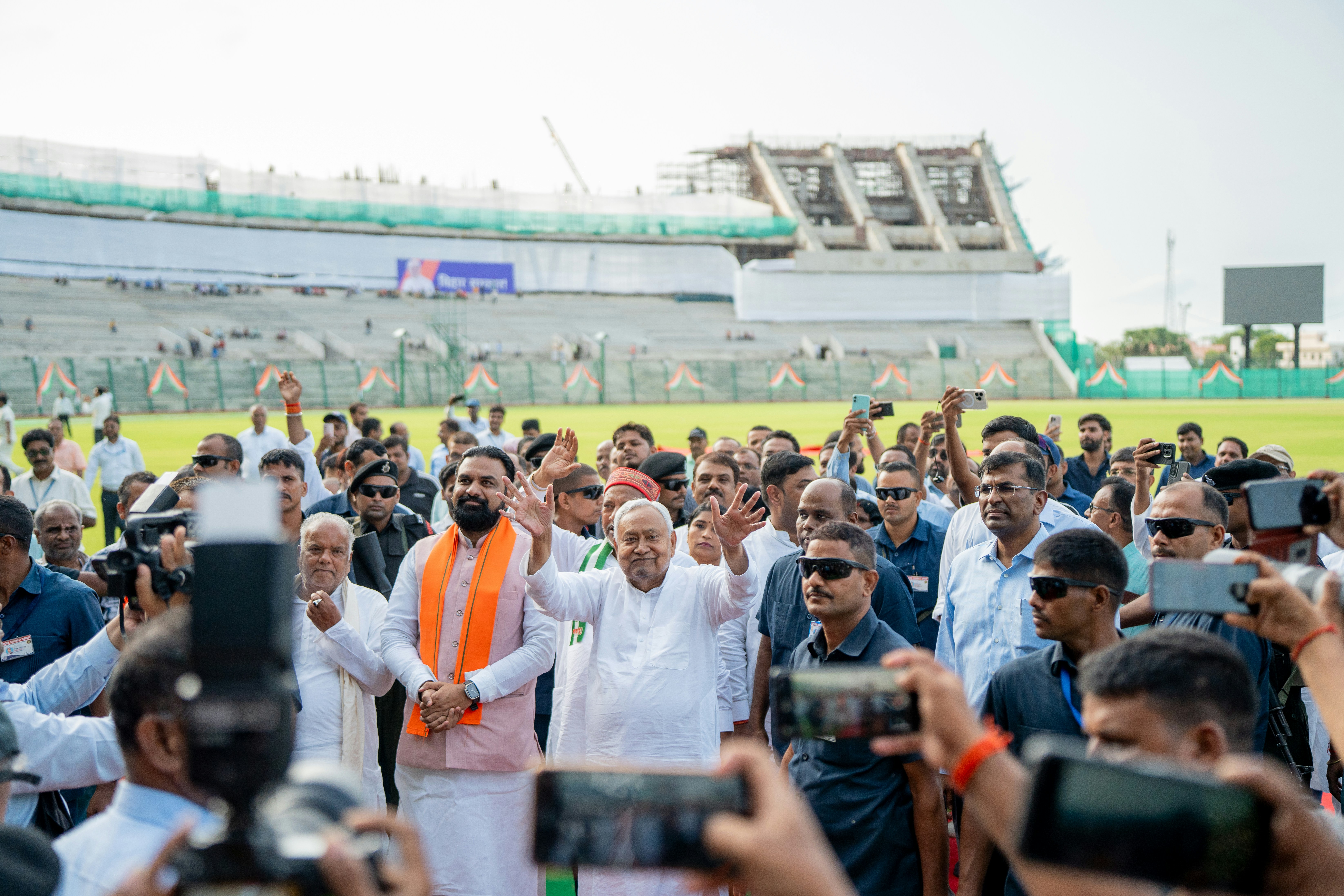 Man waving to crowd at stadium with cameras