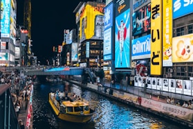 Neon signs illuminate a canal with a boat at night.