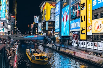 Neon signs illuminate a canal with a boat at night.