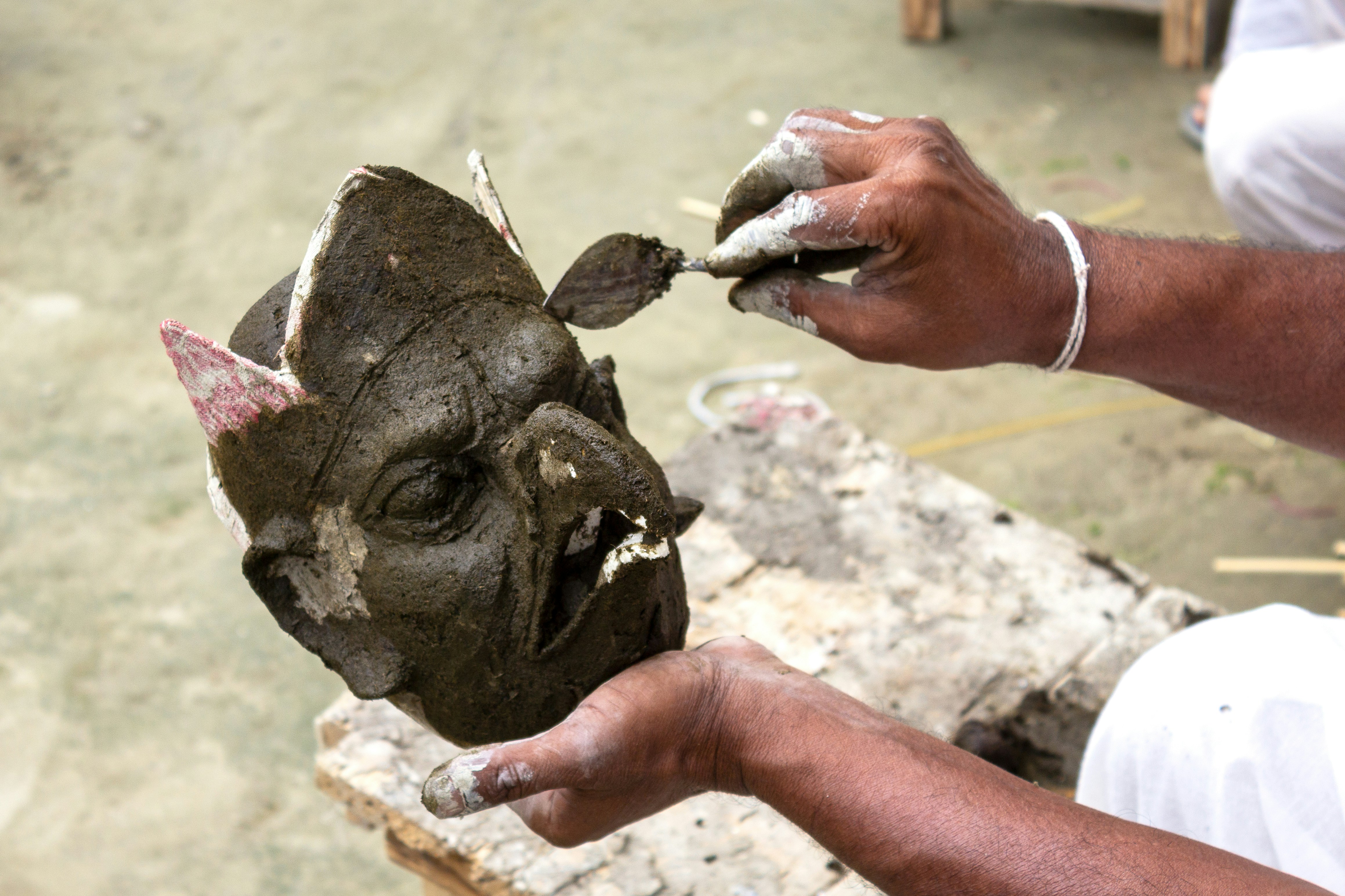 Hands sculpting a clay mask with intricate details
