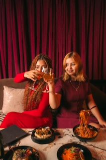 Two women toasting with wine at a table with food.