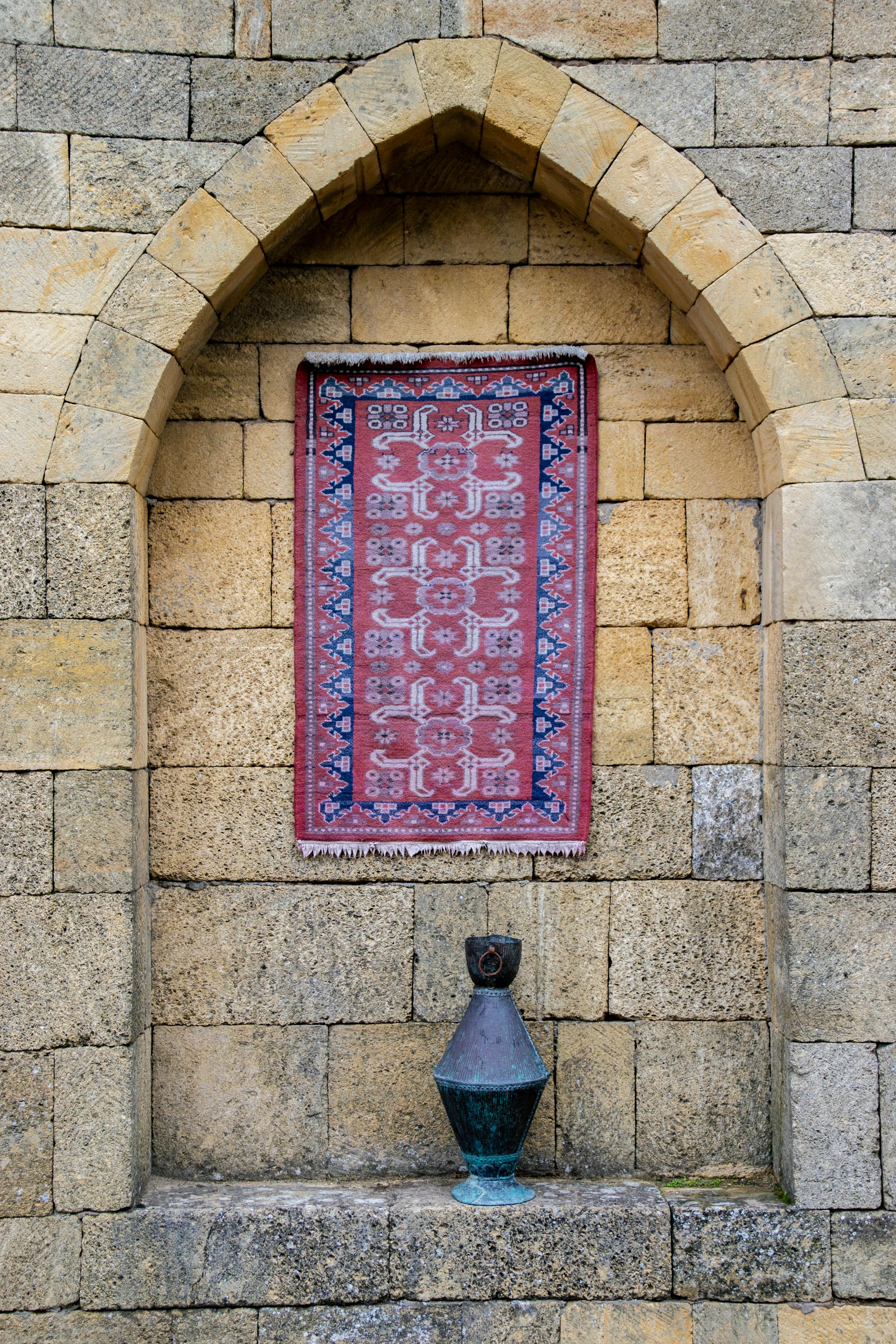 A patterned rug hangs in an arched stone alcove.