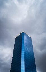Tall blue glass skyscraper against stormy clouds
