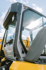Yellow excavator cab with sun glare on window.
