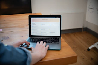 Person typing on a laptop computer on a wooden desk.