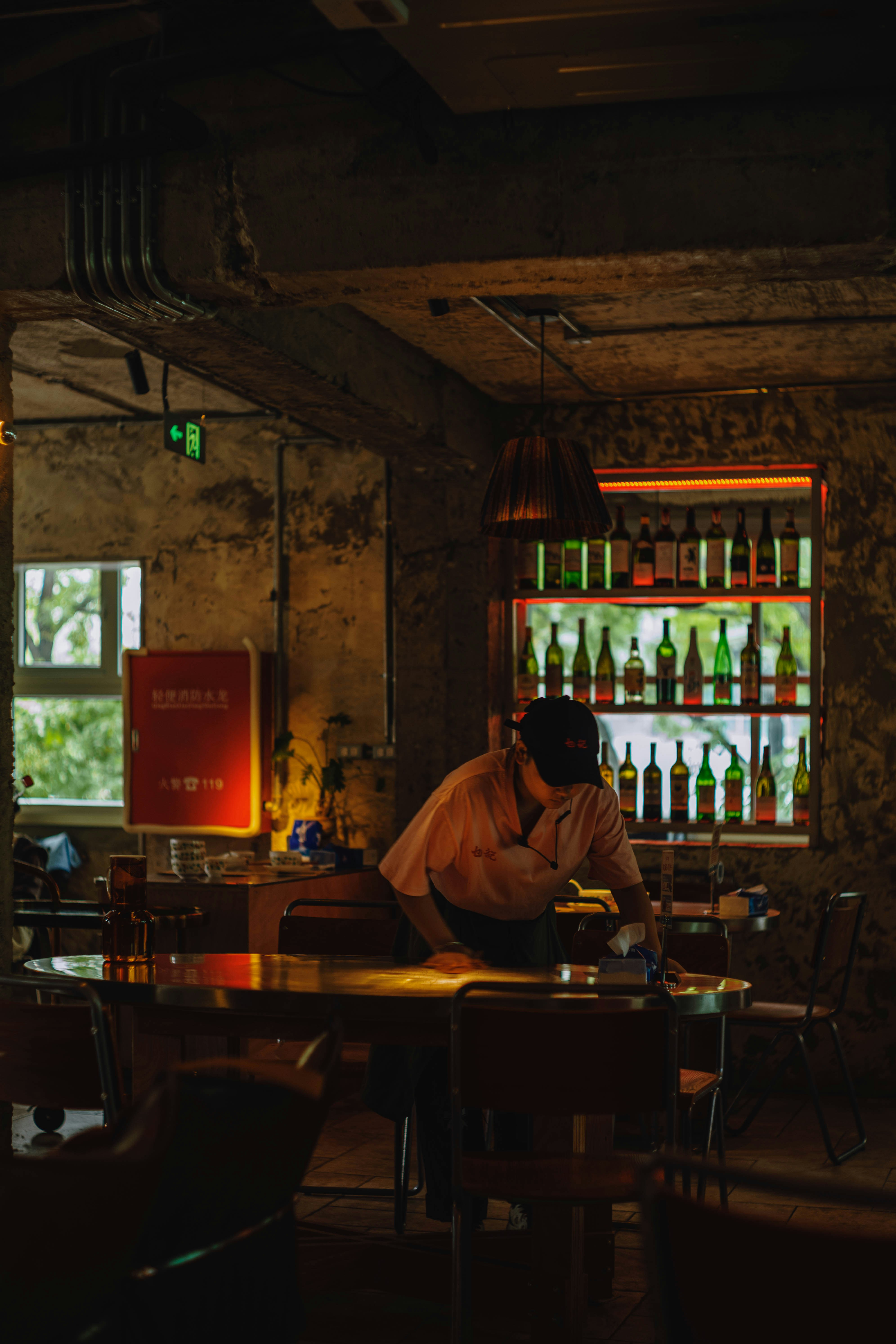 Man cleaning table in dimly lit bar with bottles