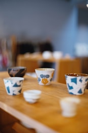 Various decorative ceramic cups on a wooden shelf.