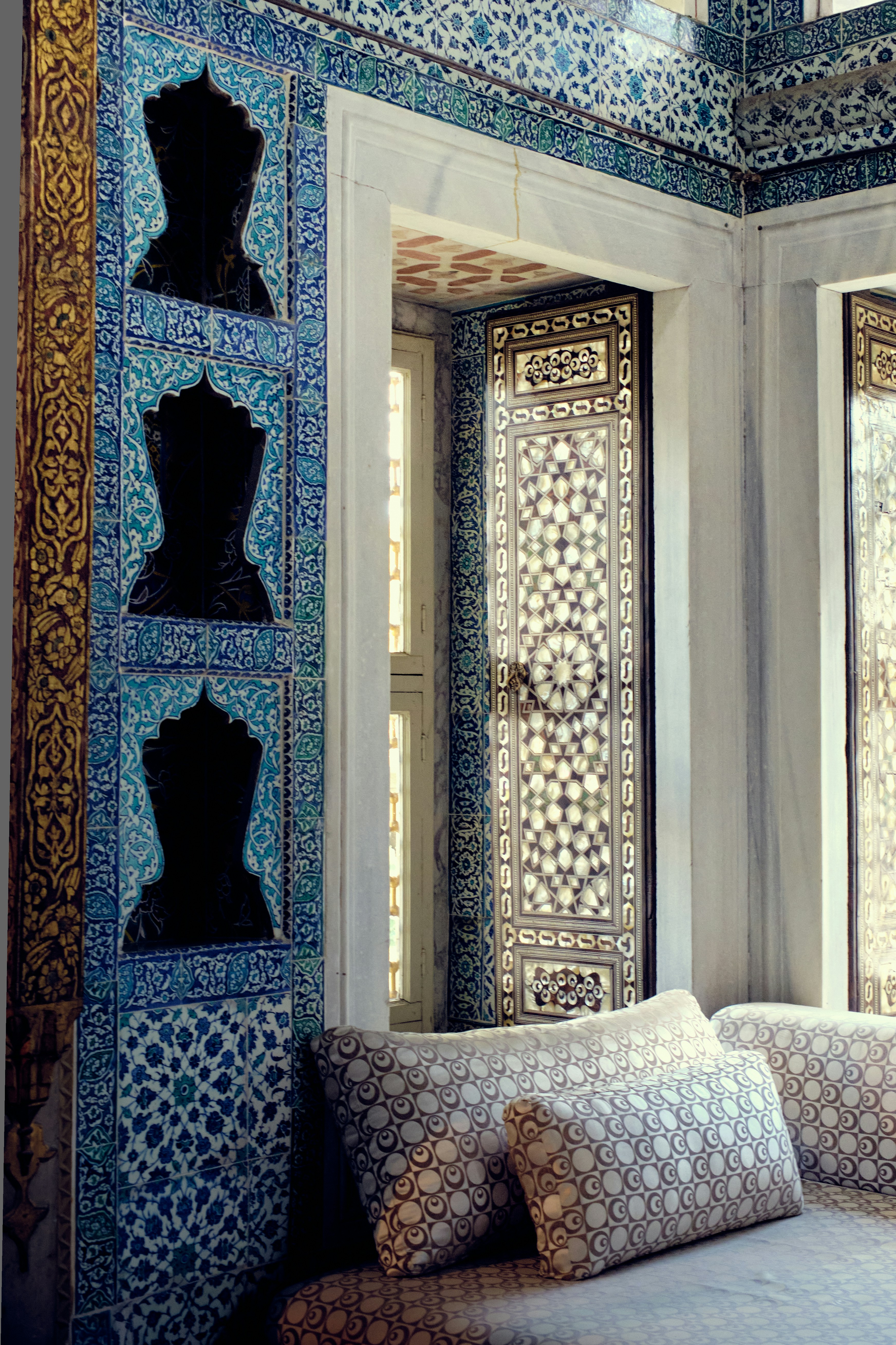 Intricate blue tilework adorns an ornate room with patterned cushions.