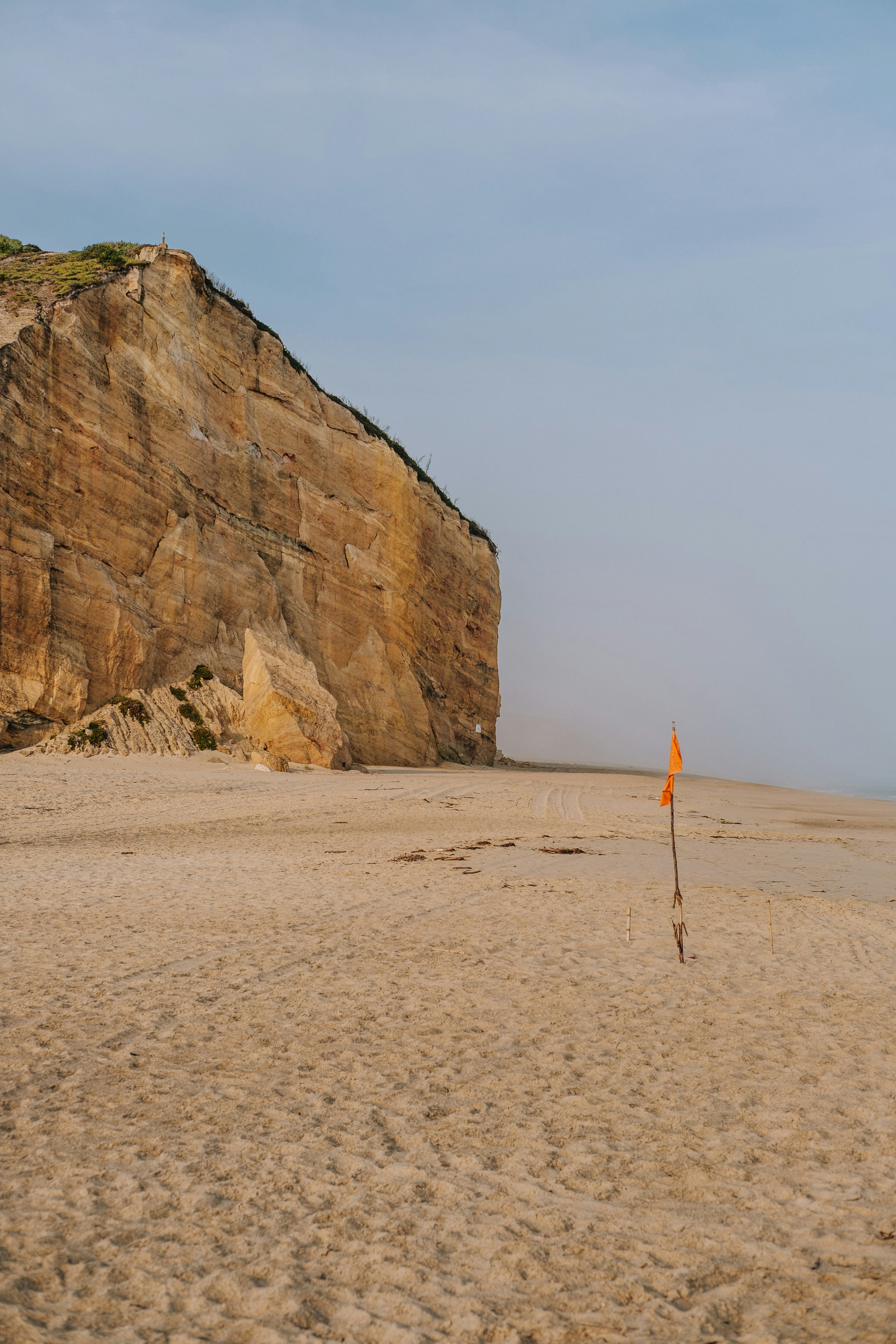 Sandy beach with a large cliff and orange flag