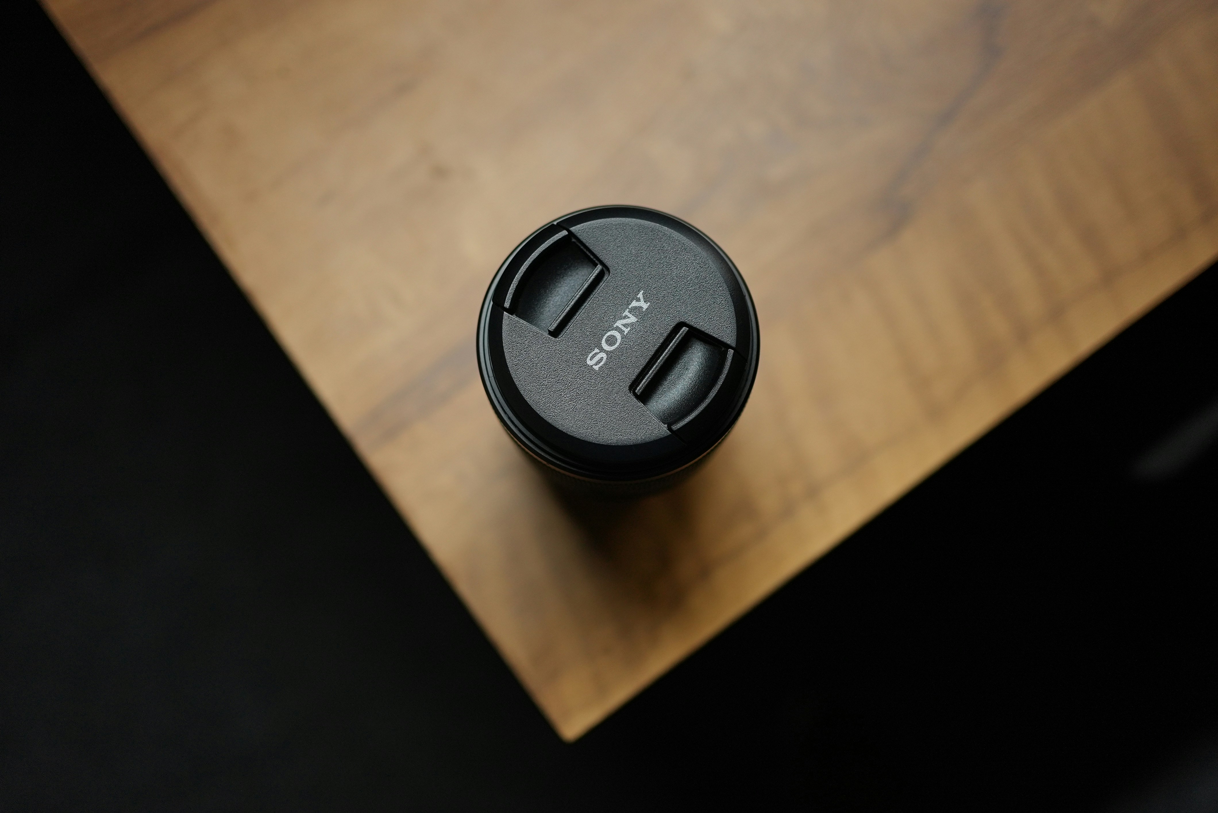 A sony lens cap on a wooden surface.