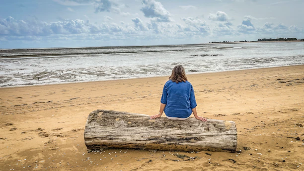 Woman sits on driftwood facing the ocean waves.