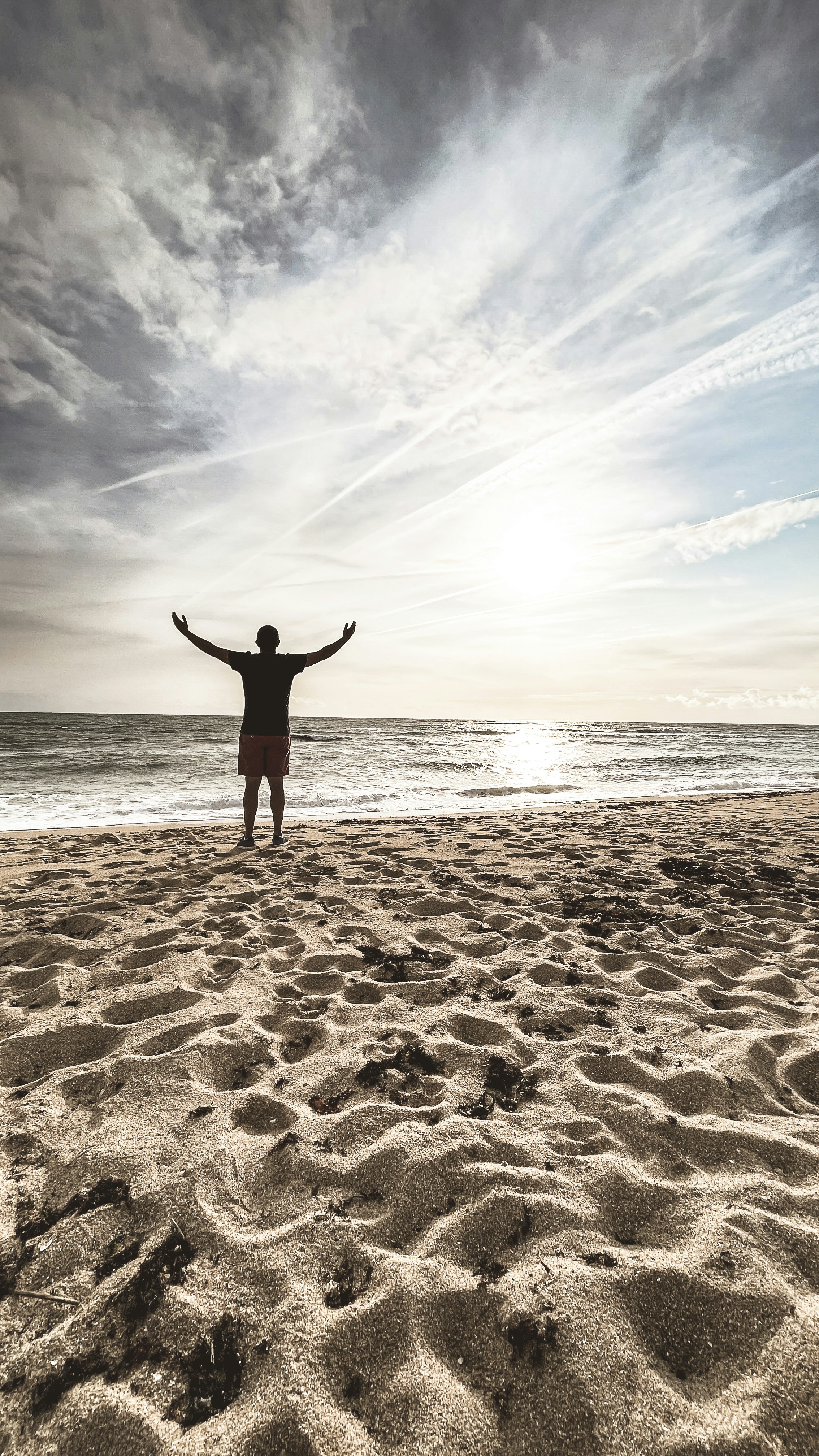 Man with arms outstretched on a sandy beach at sunset.