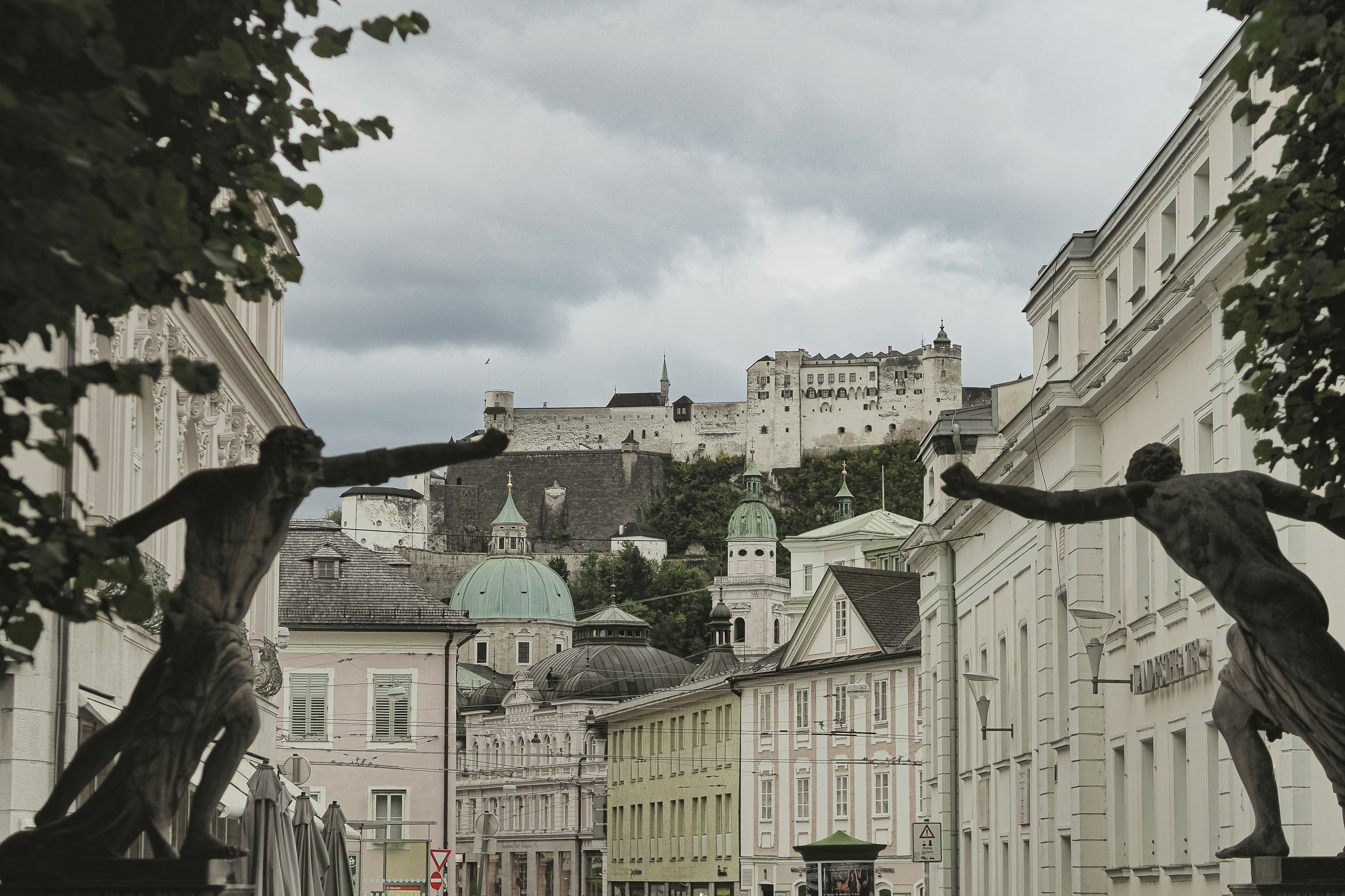 Sculptures frame historic buildings and a distant castle.