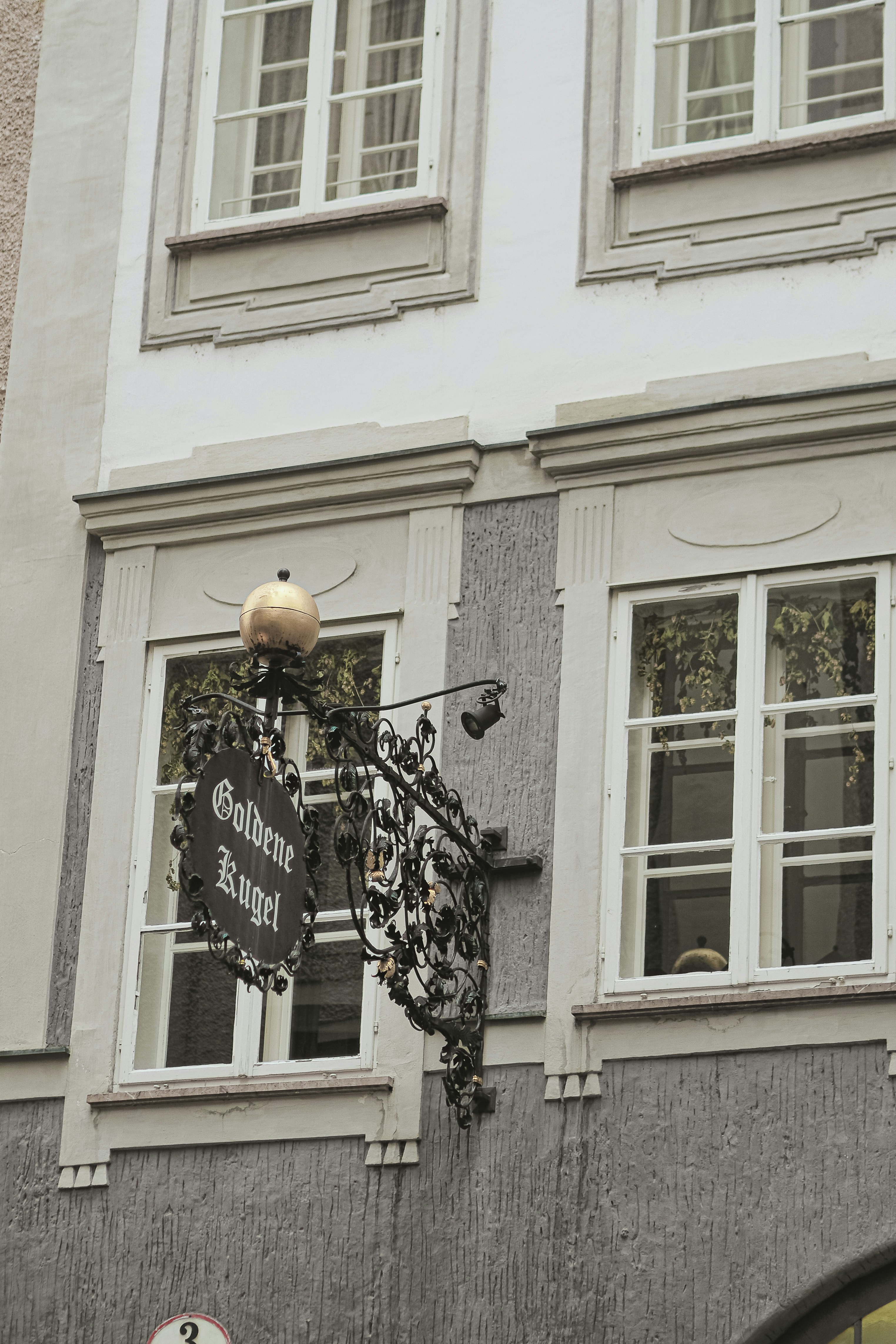 Ornate sign hangs on building facade with windows
