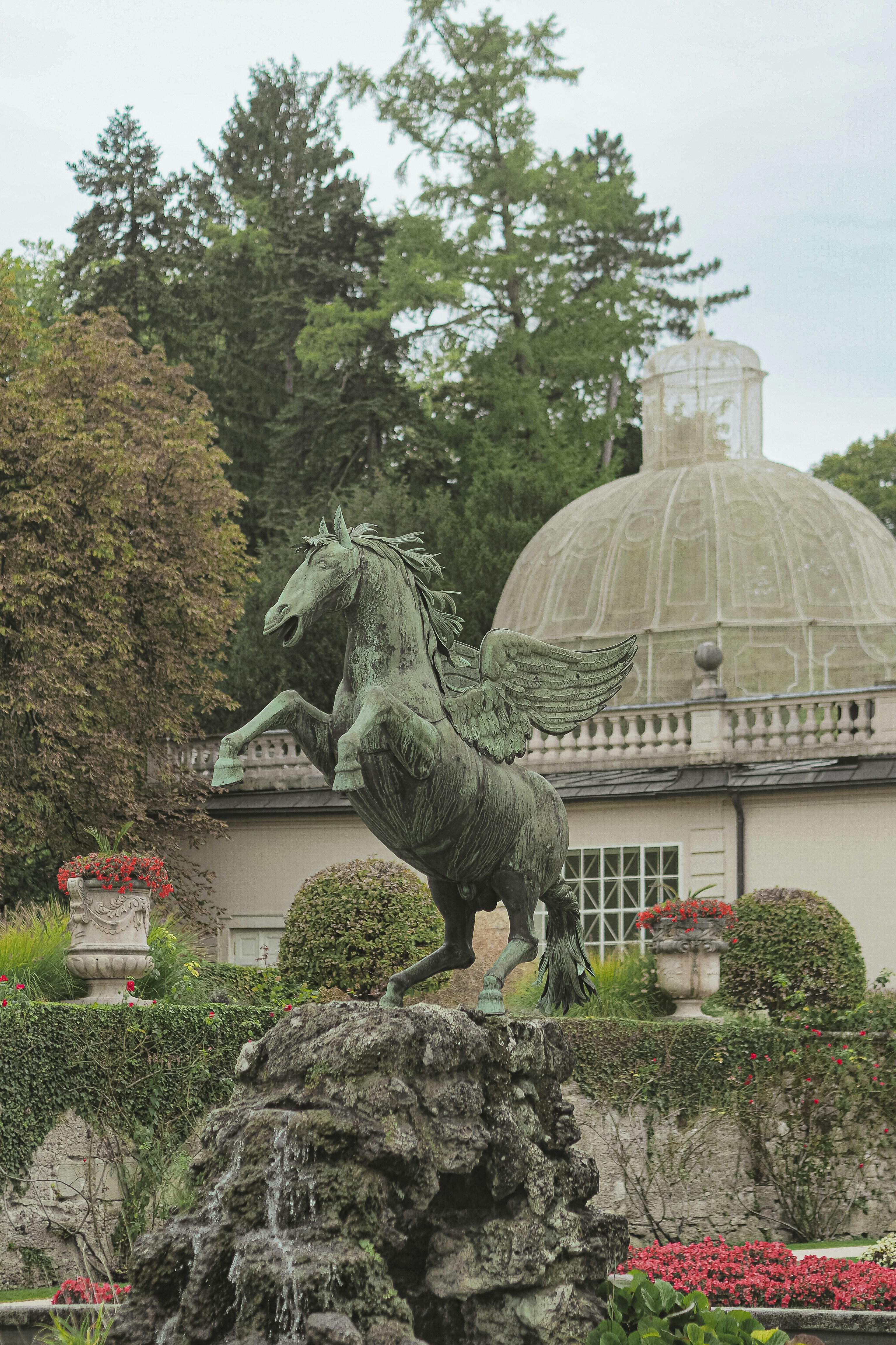 Bronze pegasus statue in a lush garden setting.