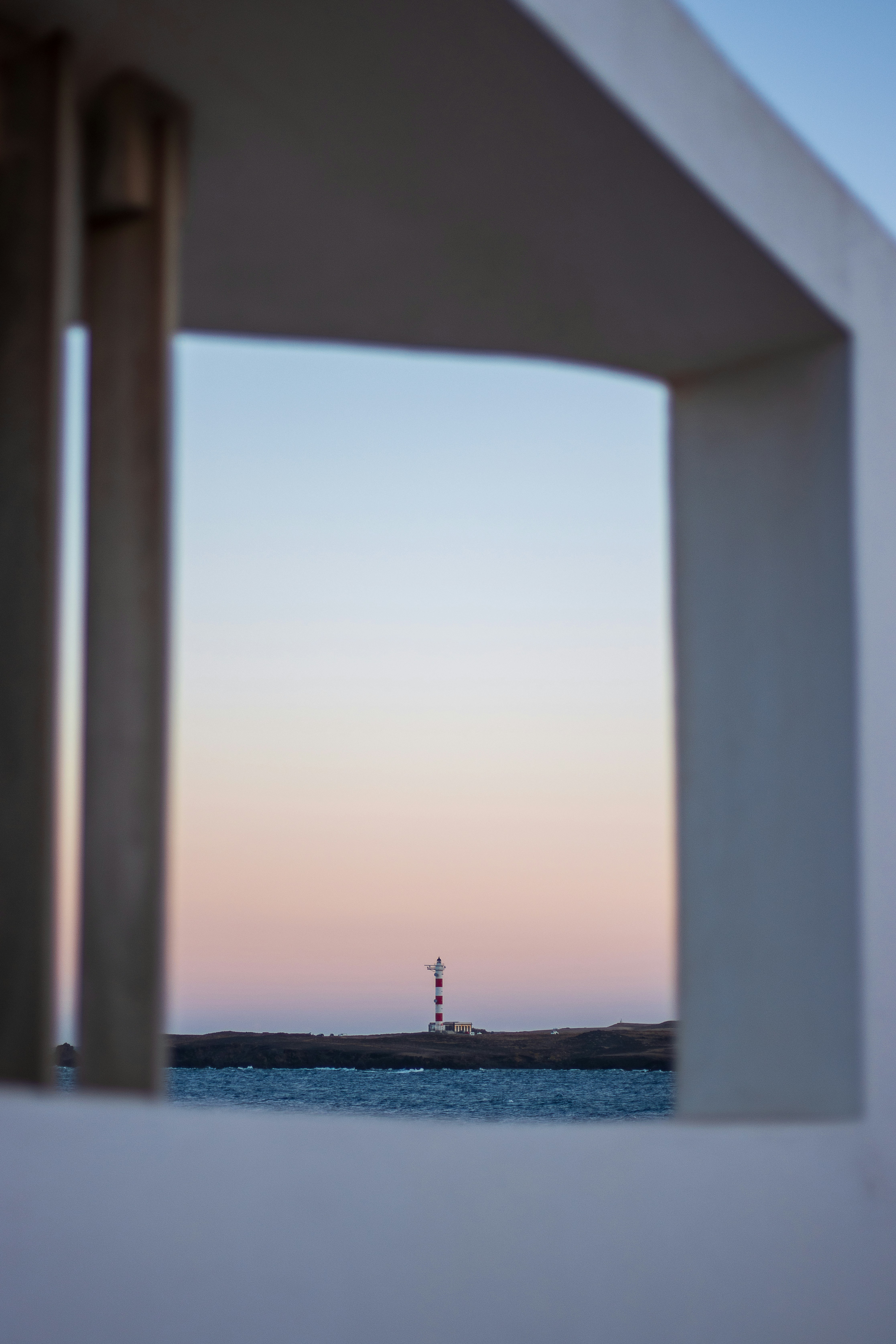 Lighthouse seen through a white architectural frame at sunset.