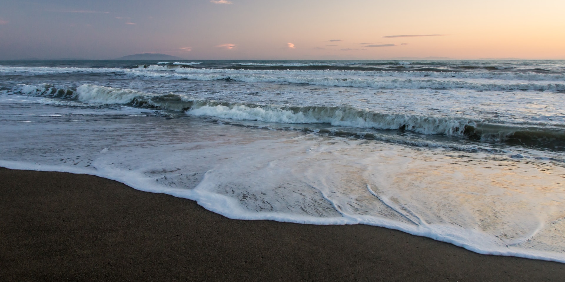 Waves gently lap onto a sandy beach at sunset.