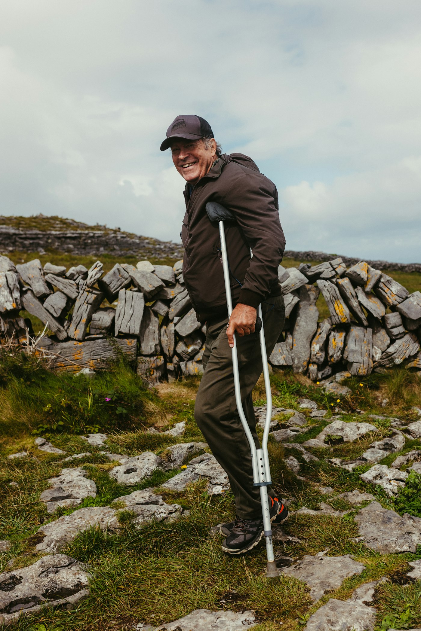 Person walking with a forearm crutch on uneven rocky terrain