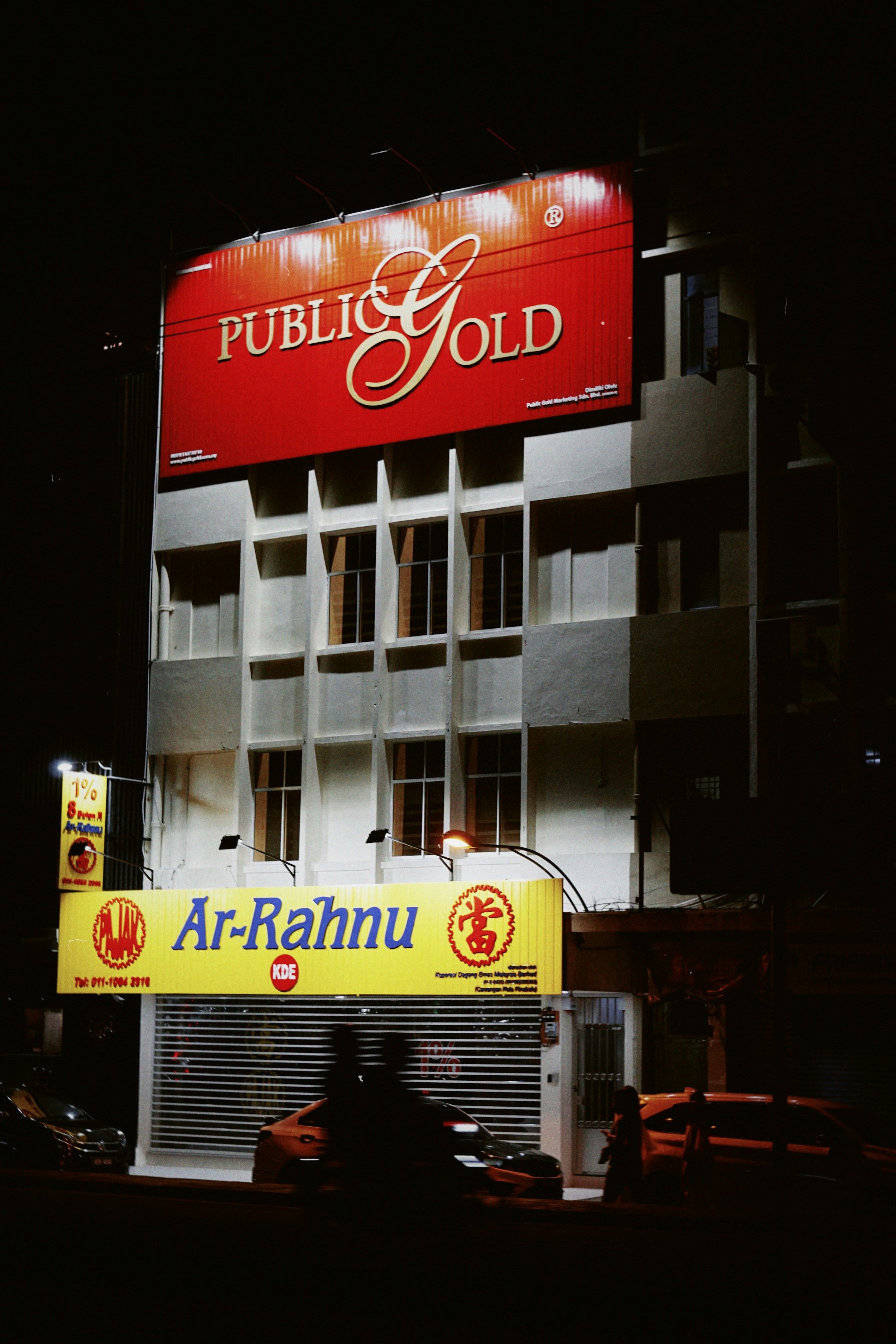 Building with "public gold" and "ar-rahnu" signs at night