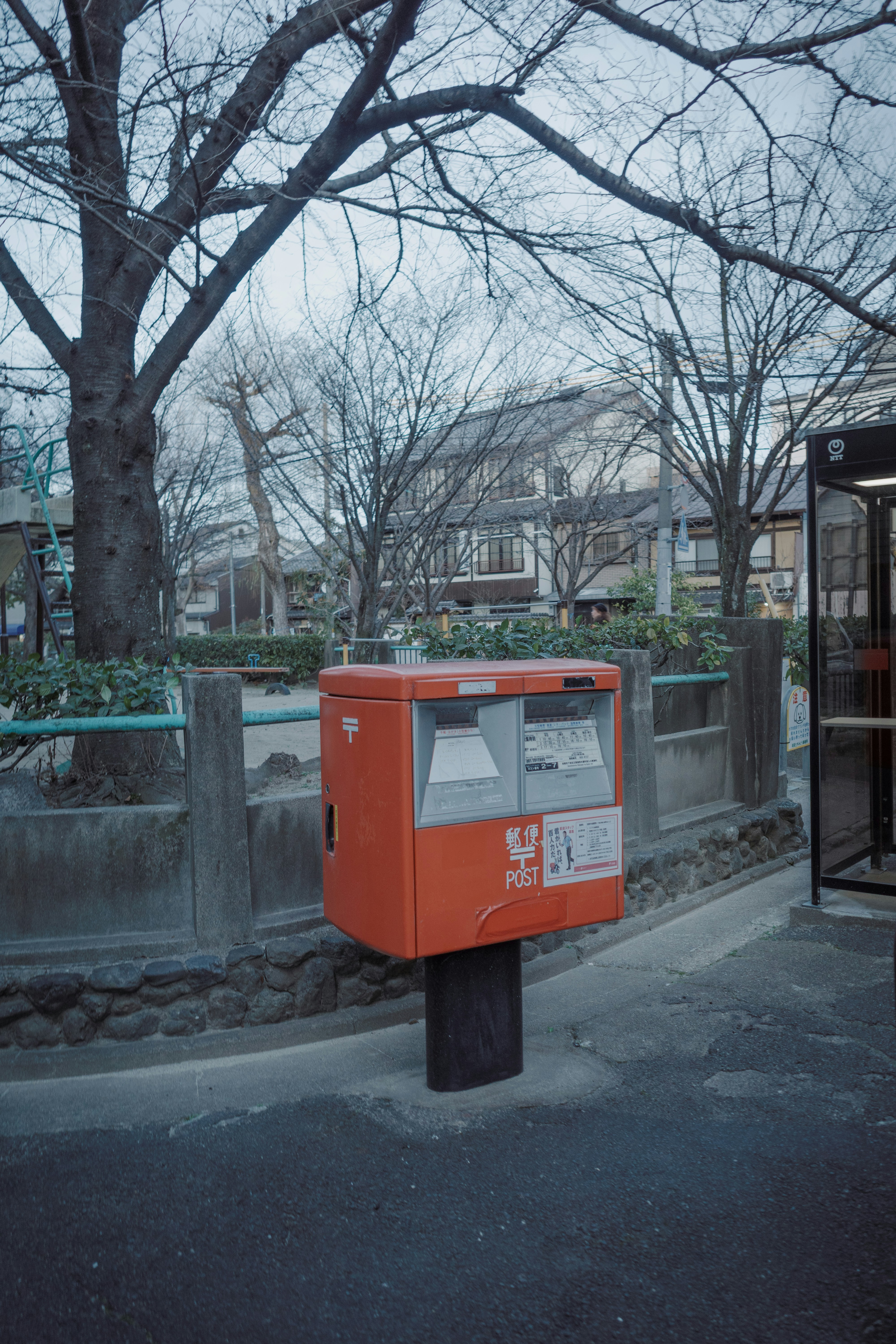 A red japanese post box stands on a sidewalk.