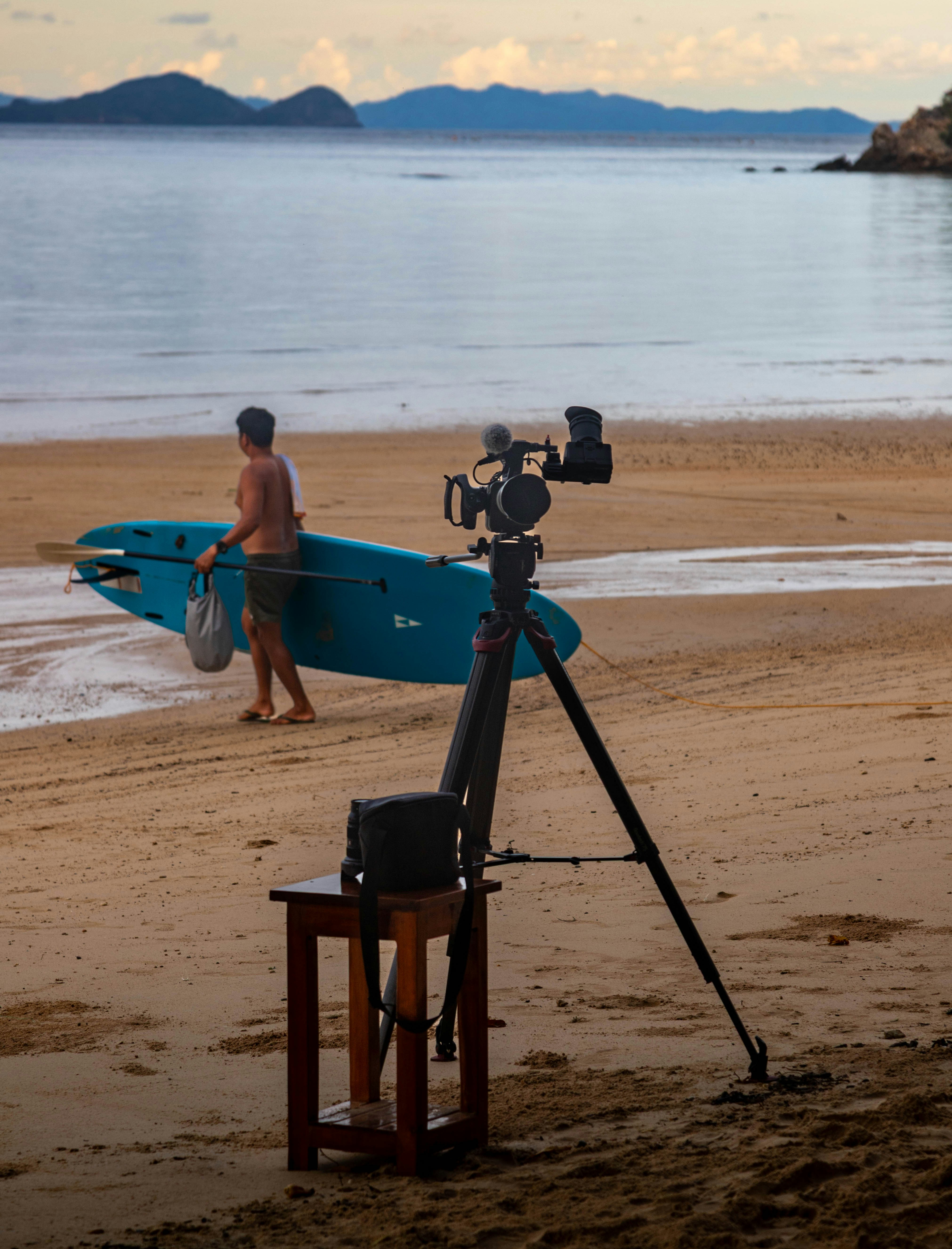 패들보드를 든 남자가 카메라 근처 해변을 걷고 있습니다.