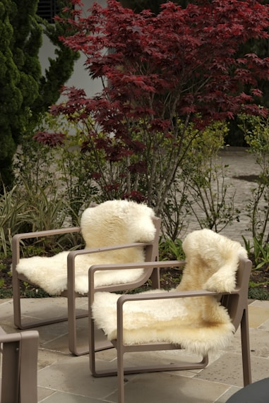 Two chairs with sheepskin throws in garden.
