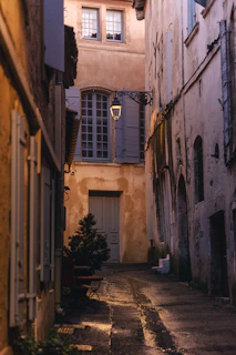 A narrow european street with a lit lantern at dusk