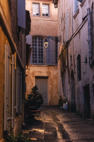 A narrow european street with a lit lantern at dusk