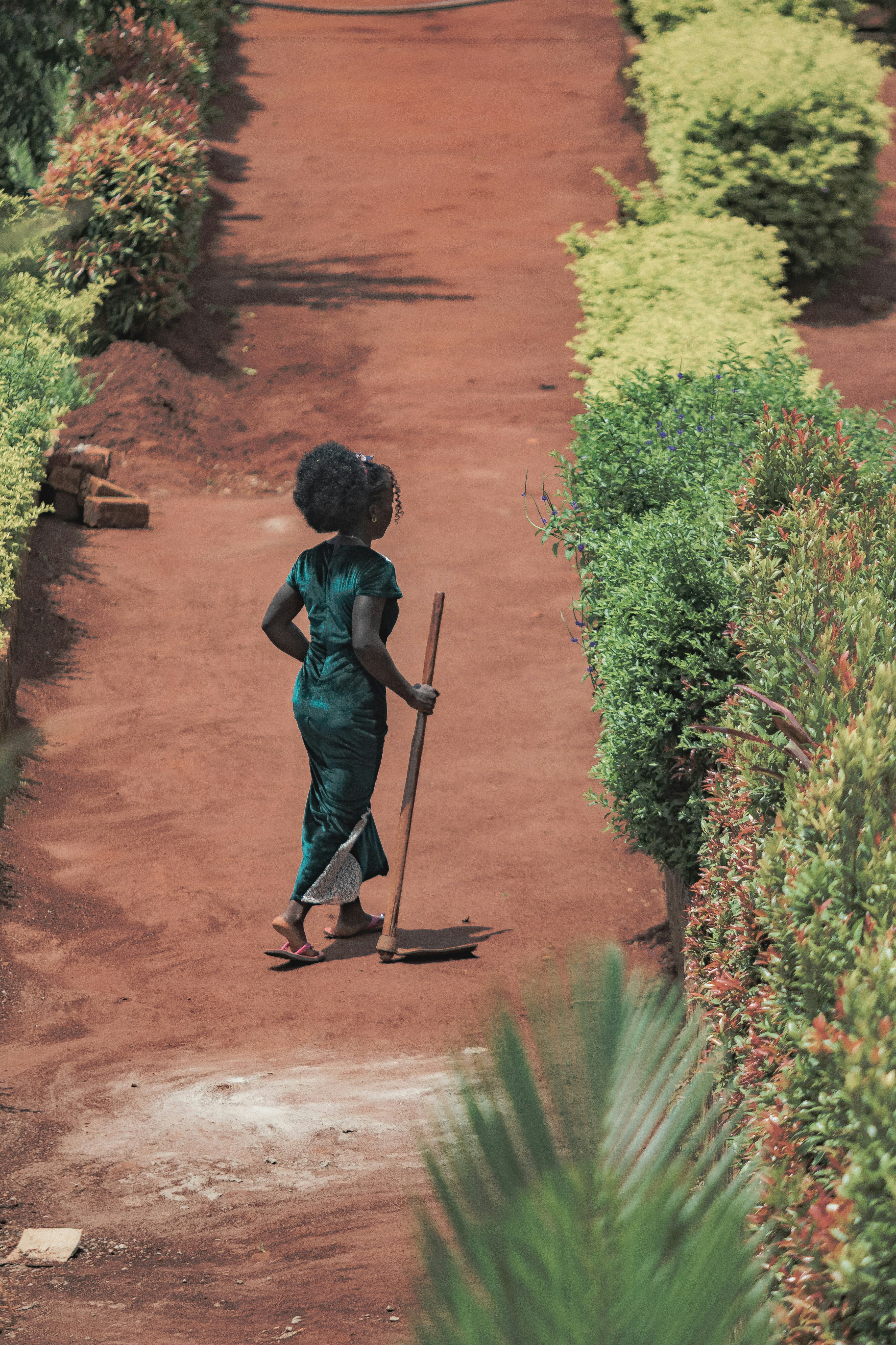 Woman with broom walking on dirt path.