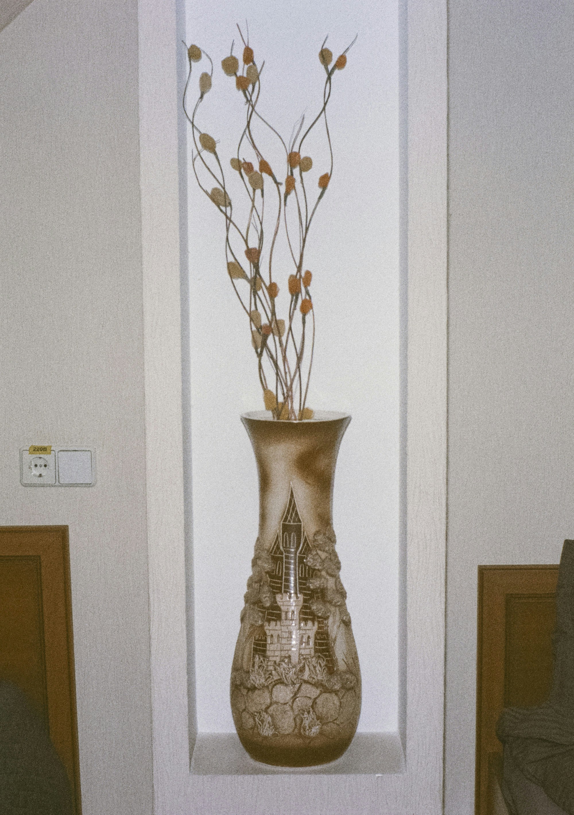 Jarrón alto con ramas decorativas en un nicho.