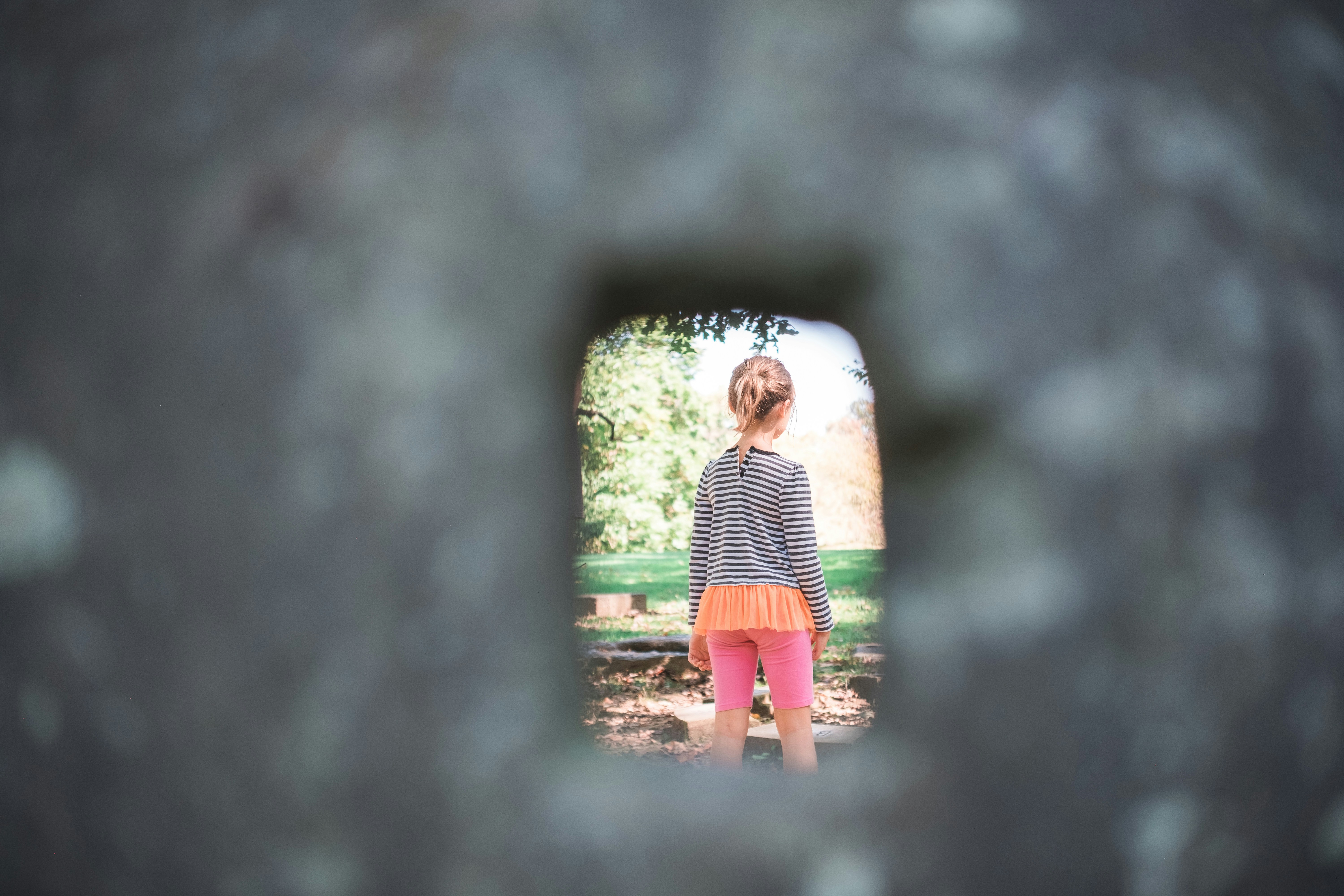 Young girl looking through a stone opening at trees