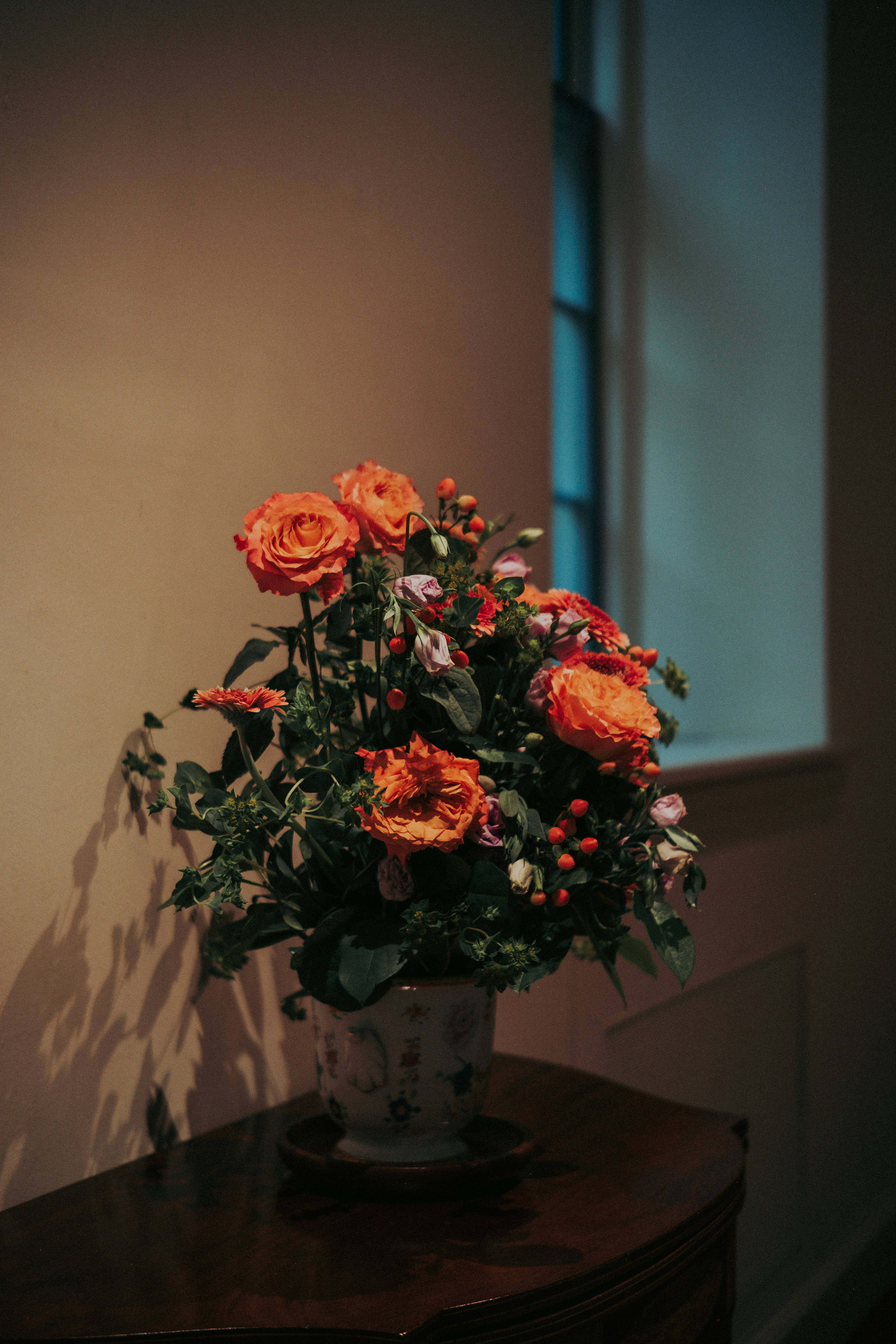 Eine Vase mit orangefarbenen Rosen und Grün im Innenbereich, Blumen im Innenbereich.