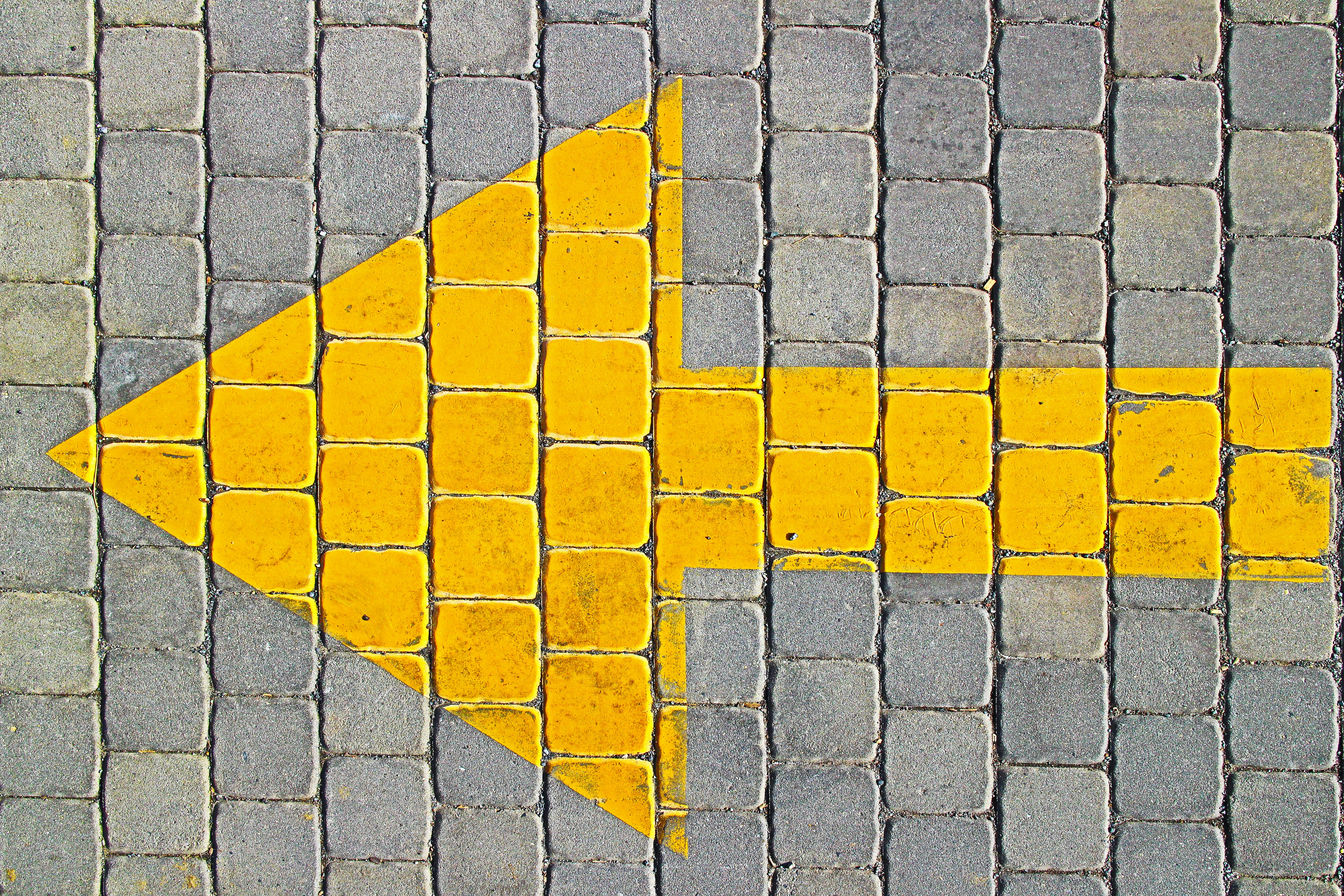 A bright yellow arrow points left on cobblestone pavement