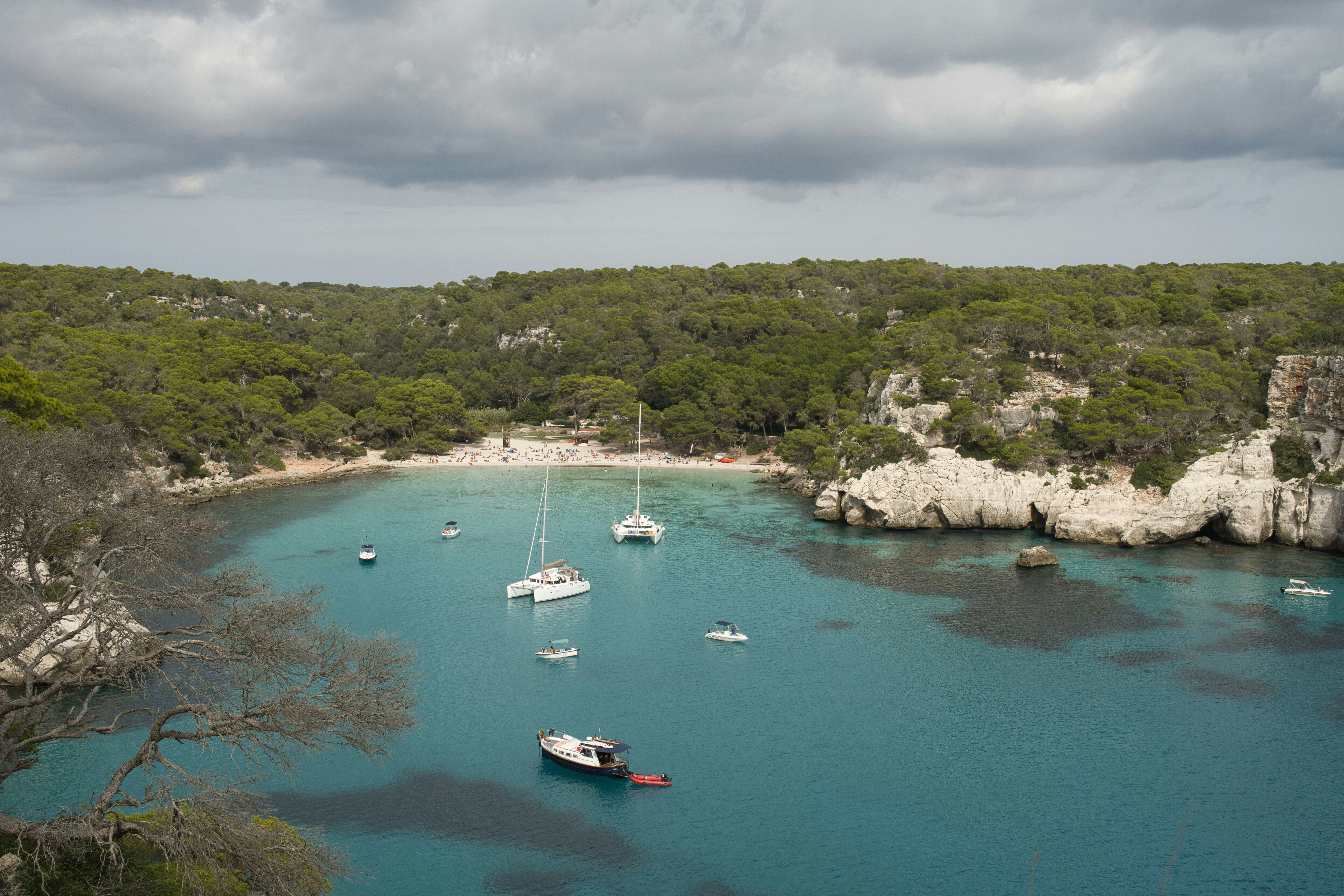 Sailboats anchored in a clear turquoise bay with rocky cliffs.