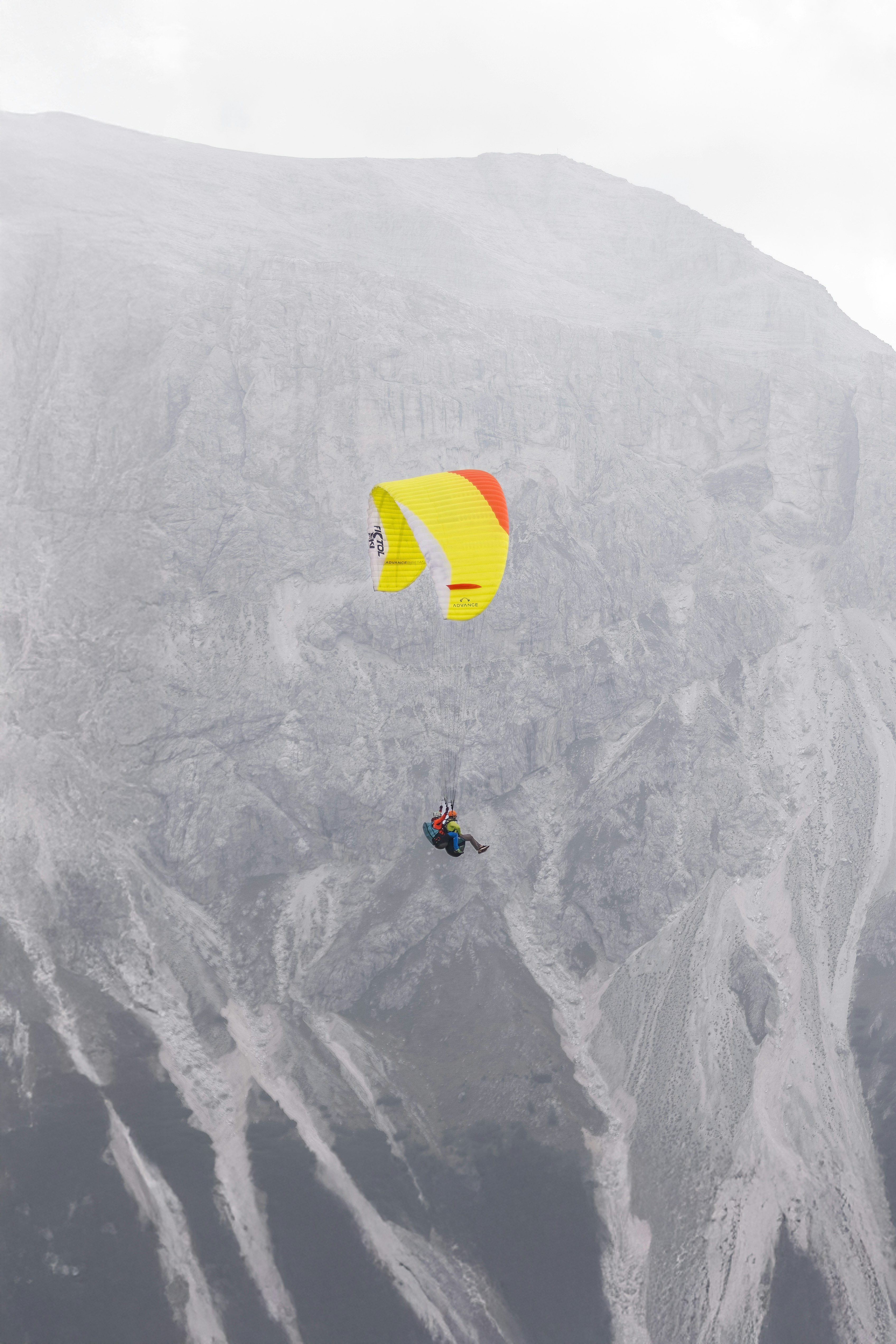 Paraglider soars against a rocky mountain backdrop.