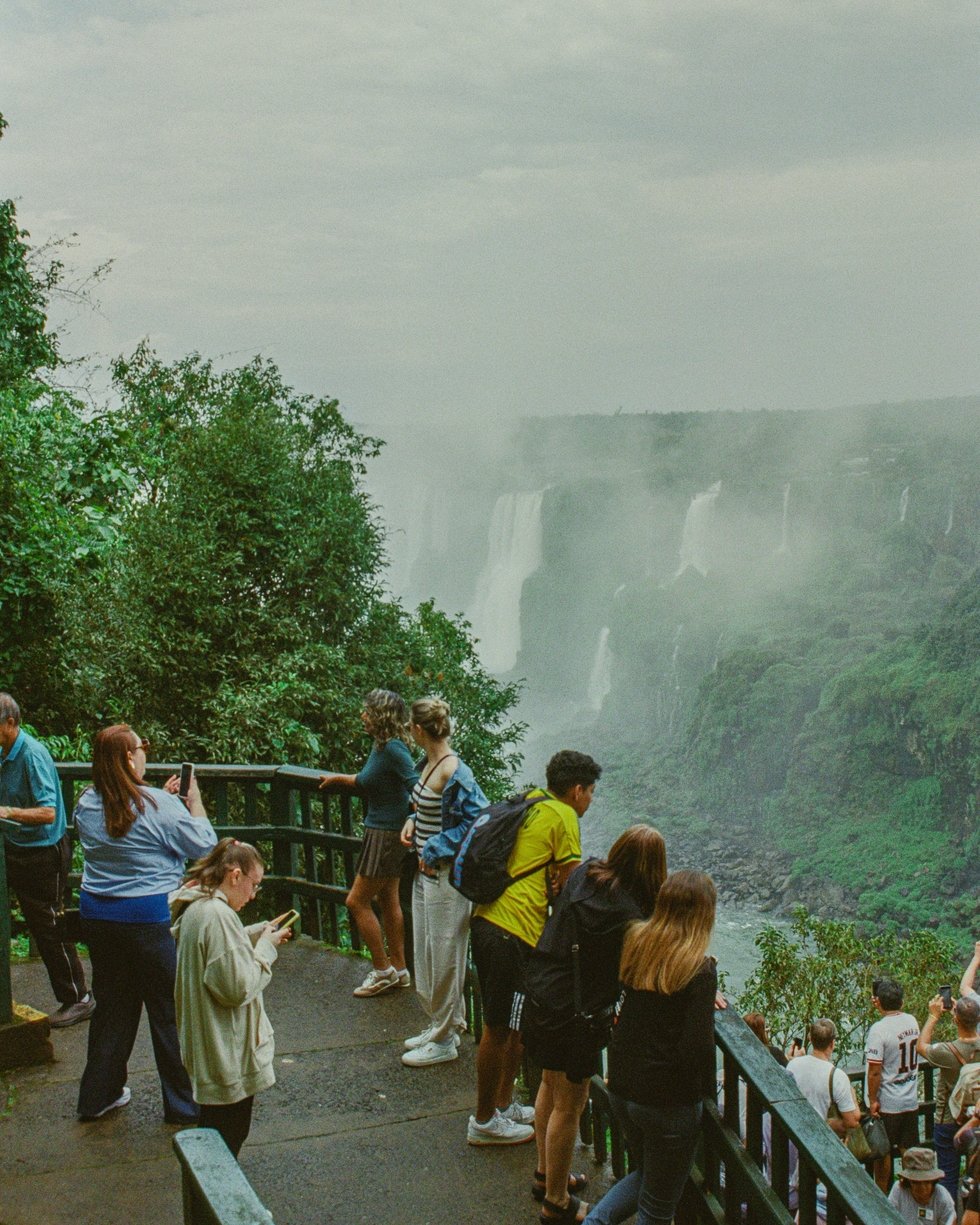 Tourists observe a misty waterfall cascading down cliffs.