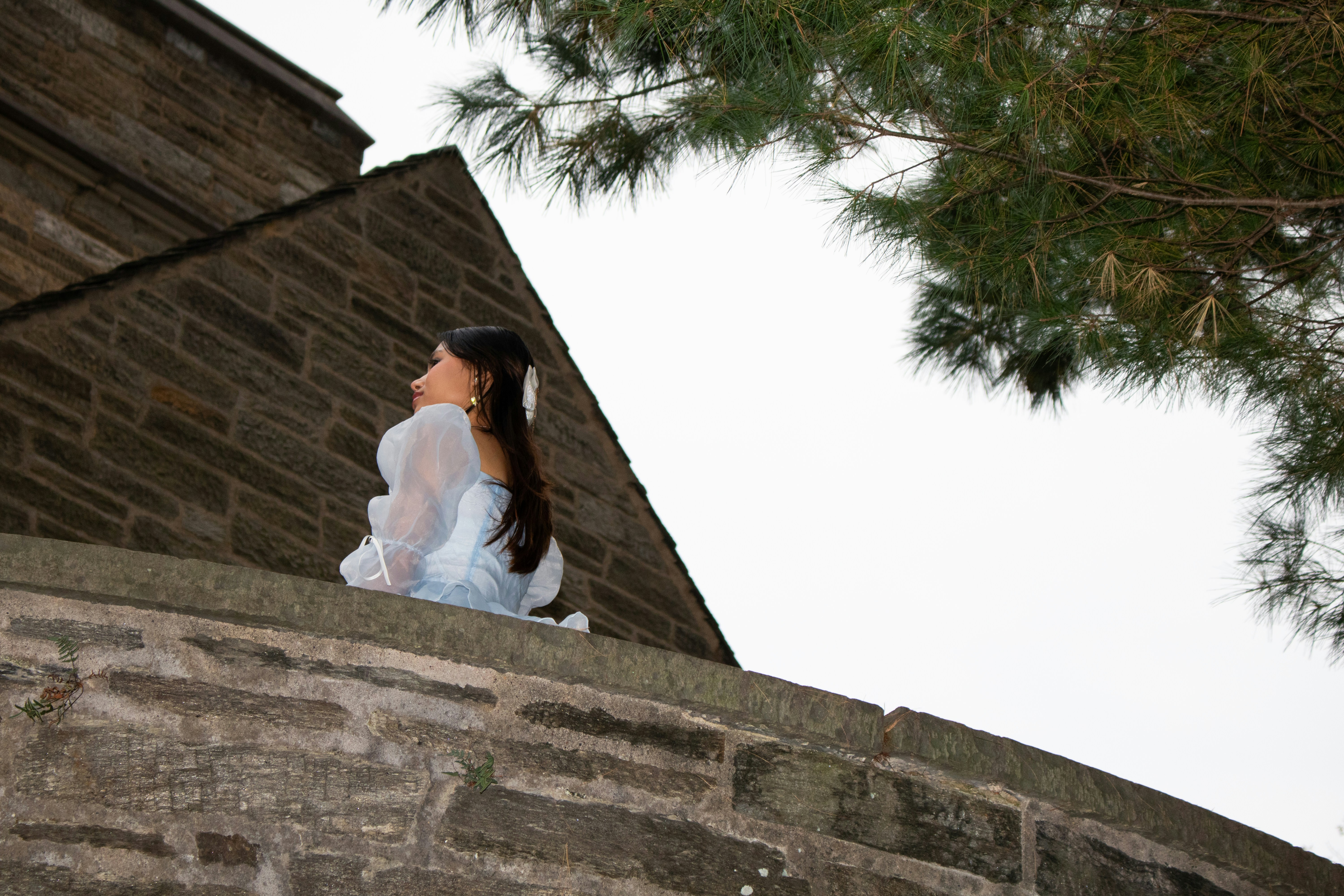 Young woman sits on stone wall under tree branches