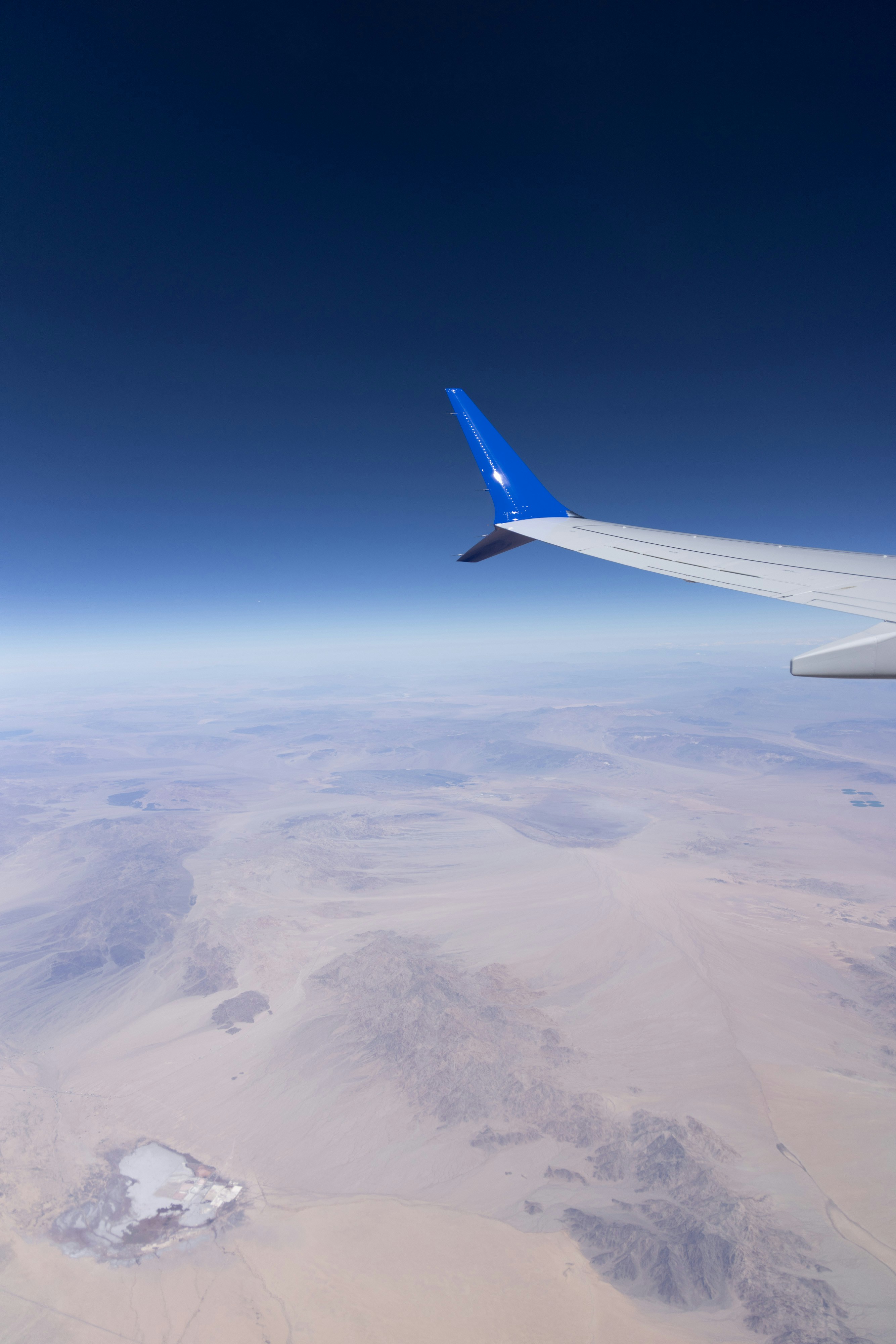 Asa de avião voando sobre uma vasta paisagem desértica.