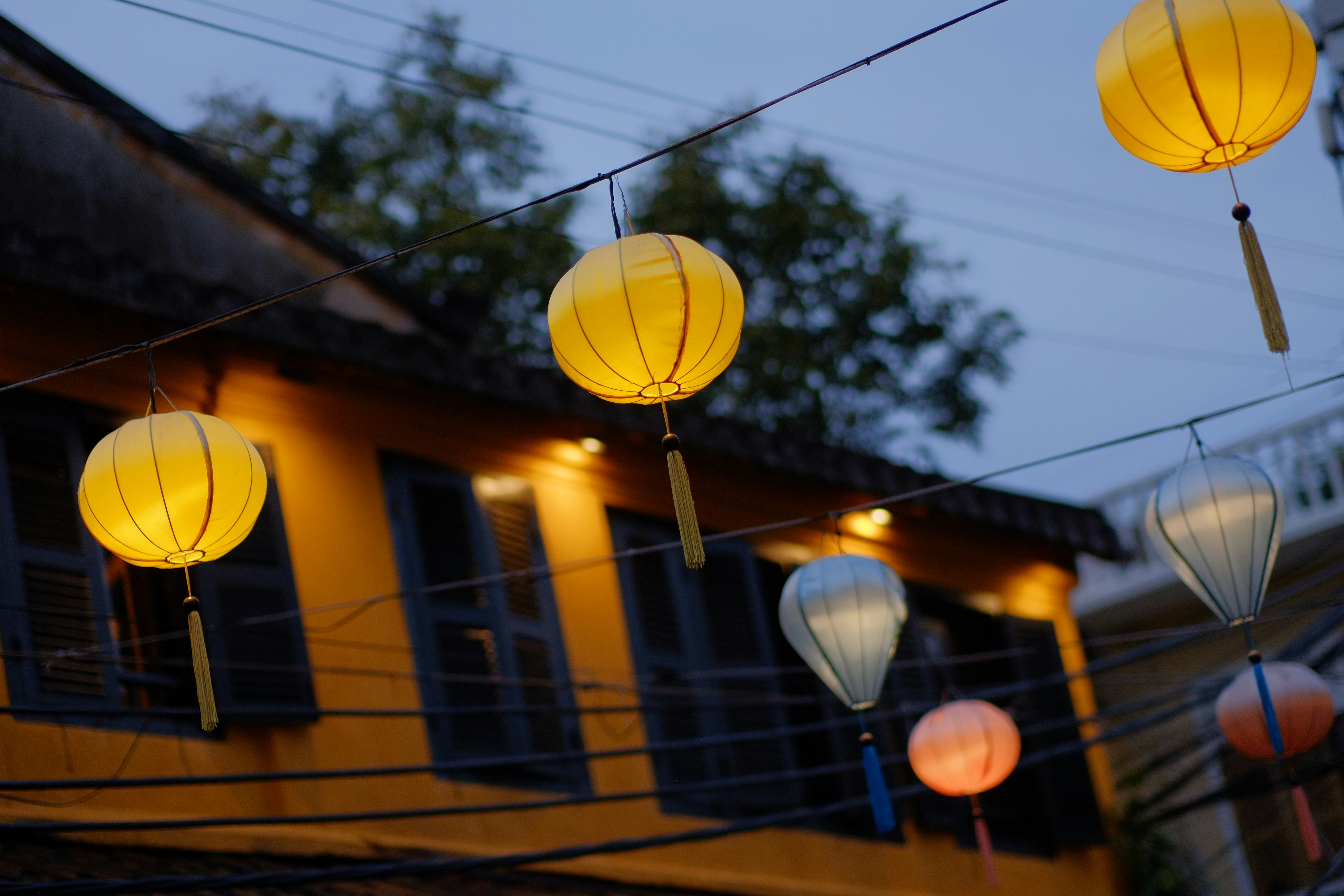 Yellow lanterns hang in front of a building at dusk.
