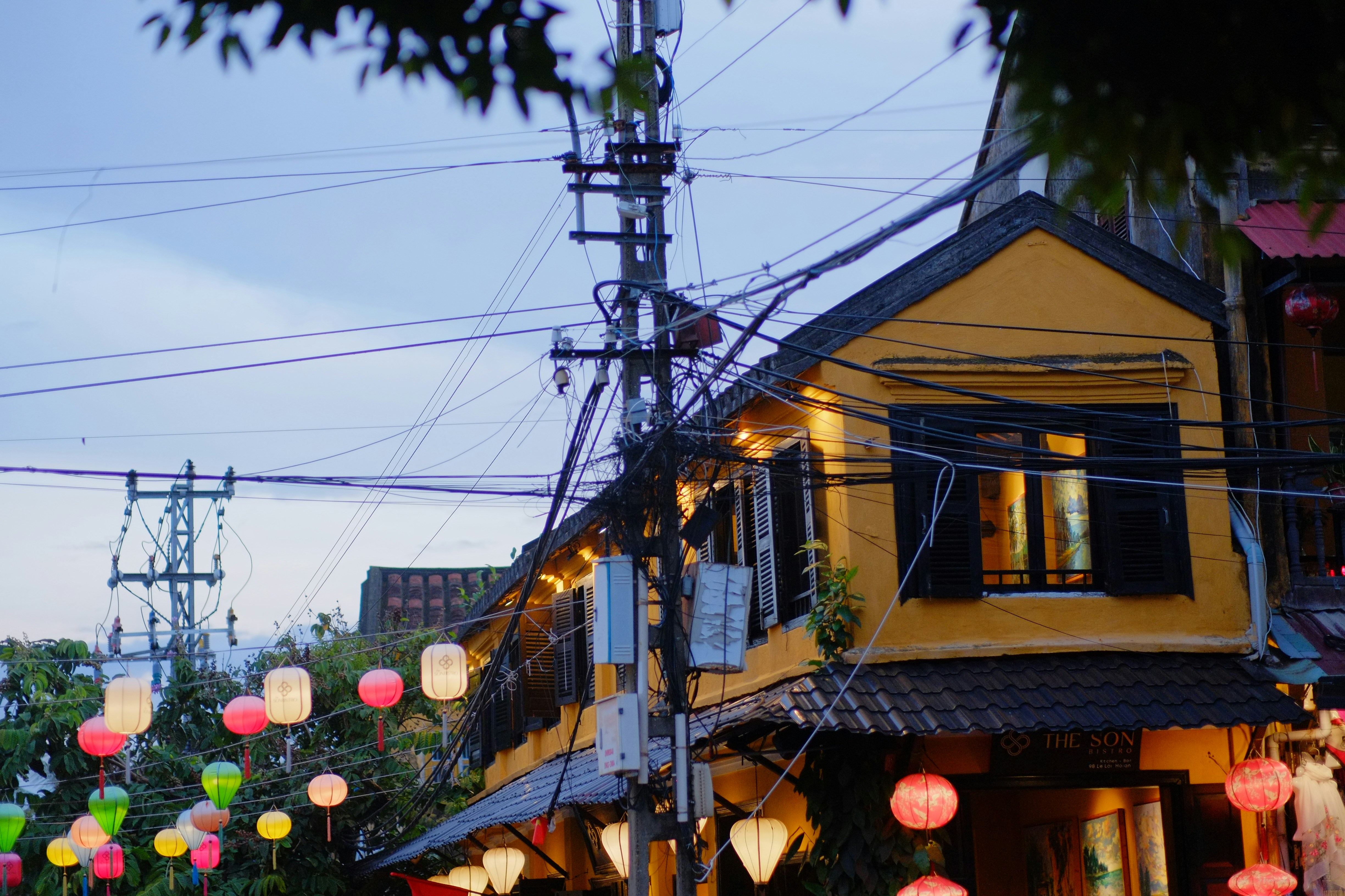 Colorful lanterns hang outside a yellow building at dusk.