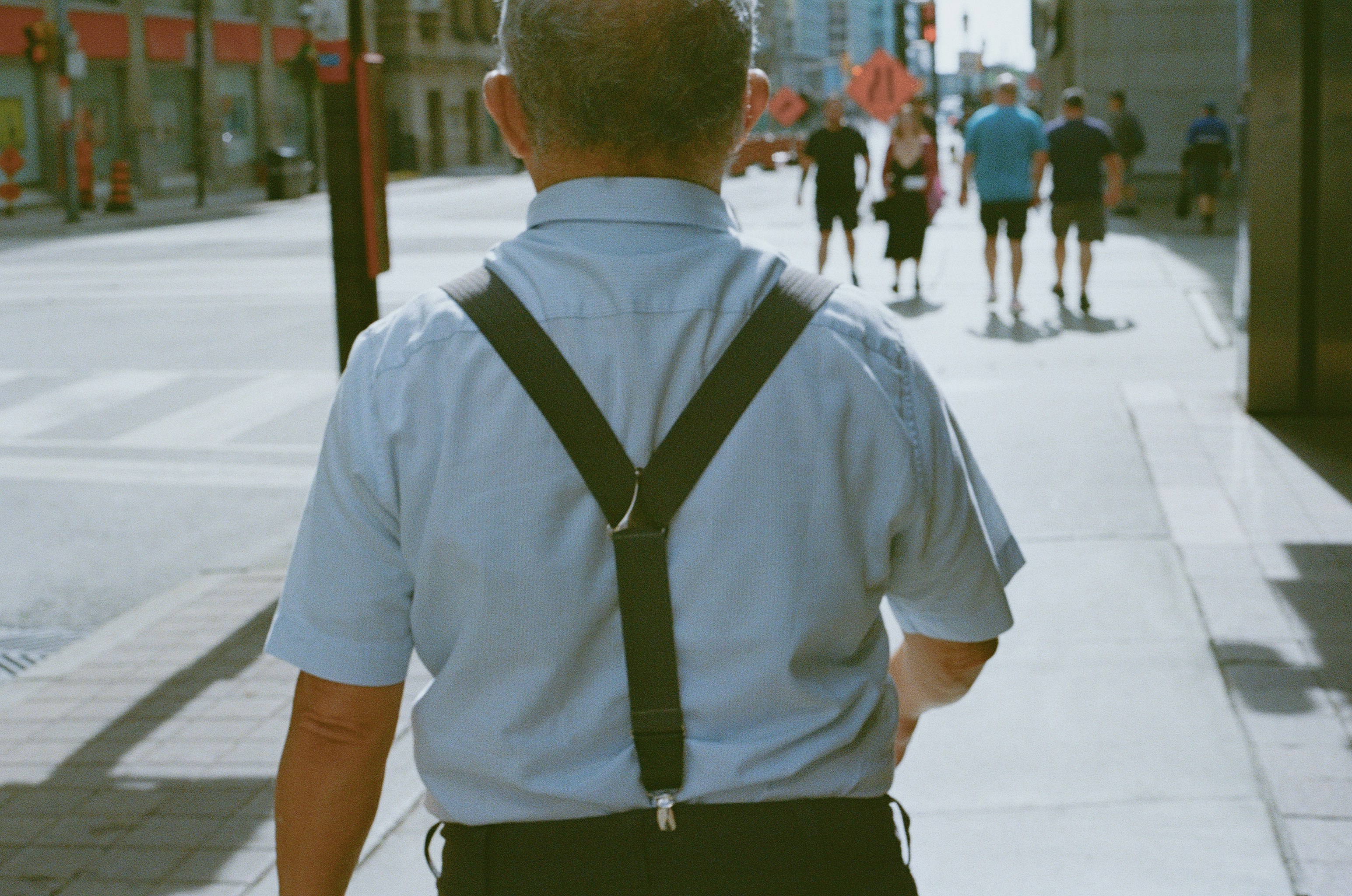 Man in suspenders walks down a city sidewalk